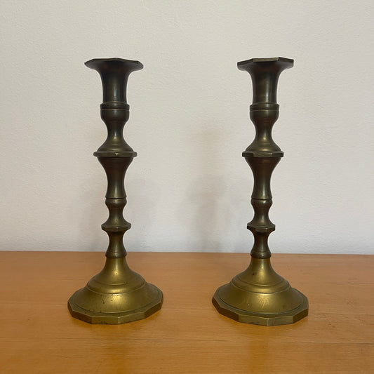 Two brass candlesticks on a wooden surface with a white background