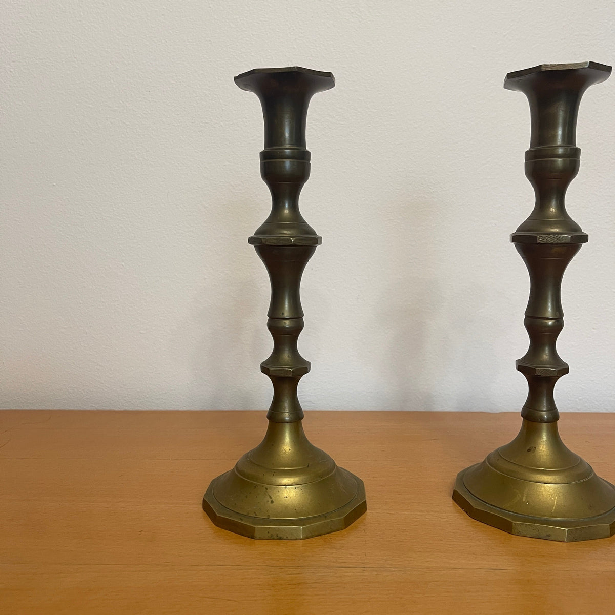 Two brass candlesticks on a wooden surface with a white background