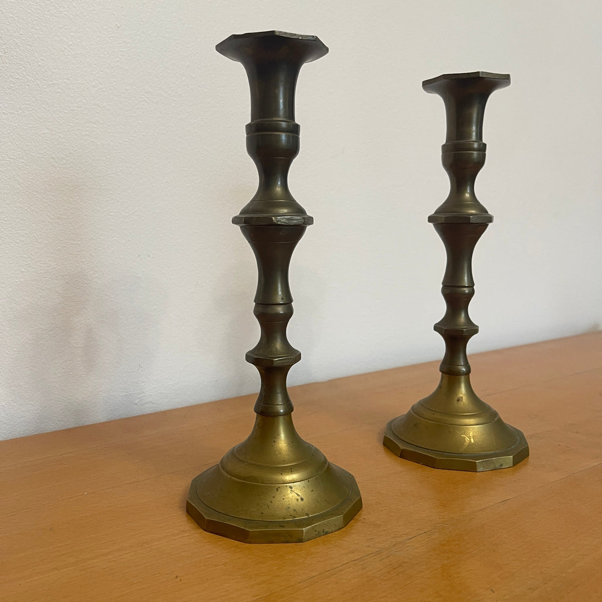 Two brass candlesticks on a wooden surface with a white background