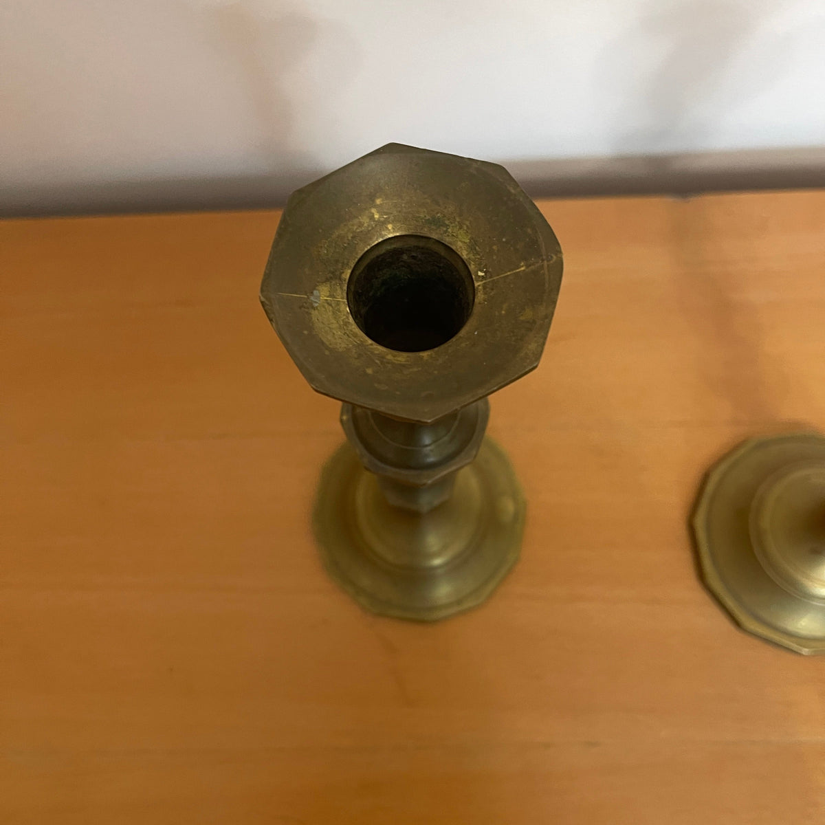 Brass candlestick on a wooden surface with a white wall background