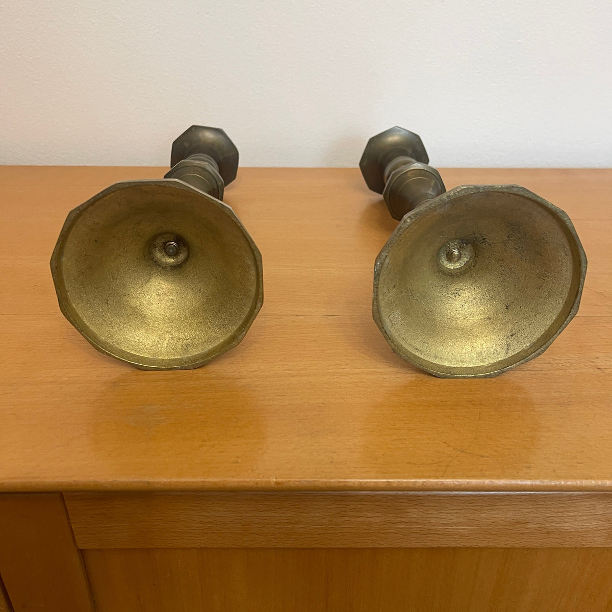 Two brass candle holders on a wooden surface with a white background
