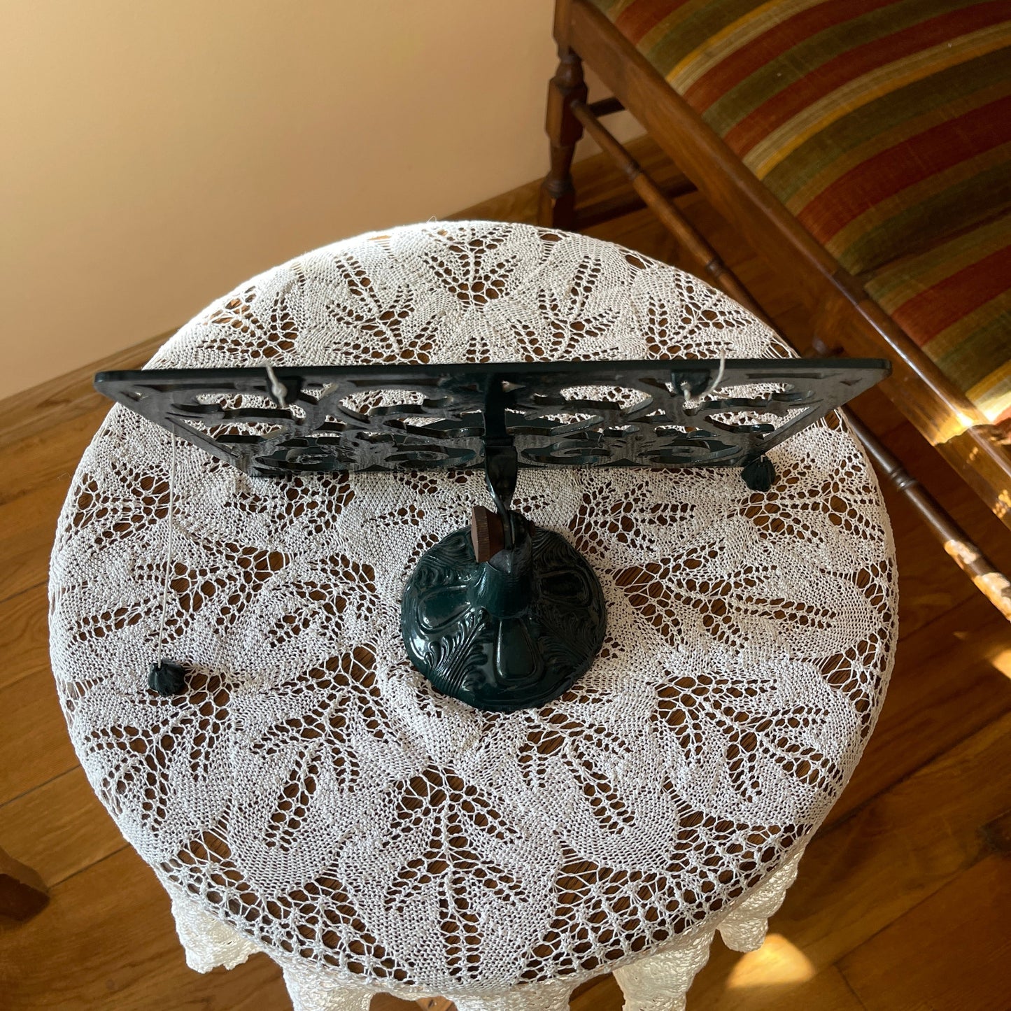 Round table with a lace tablecloth and decorative metal stand on a wooden floor.