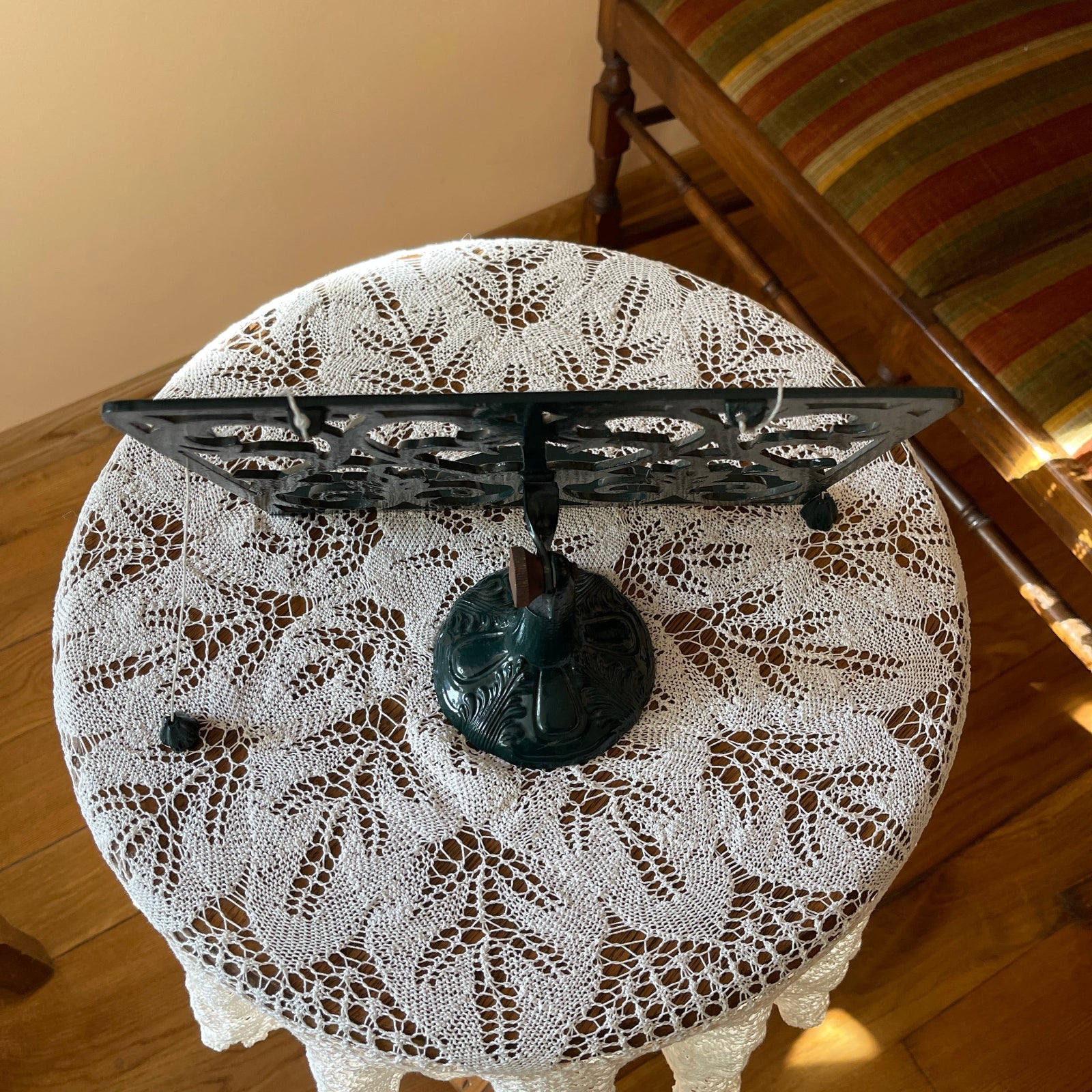 Round table with a lace tablecloth and decorative metal stand on a wooden floor.