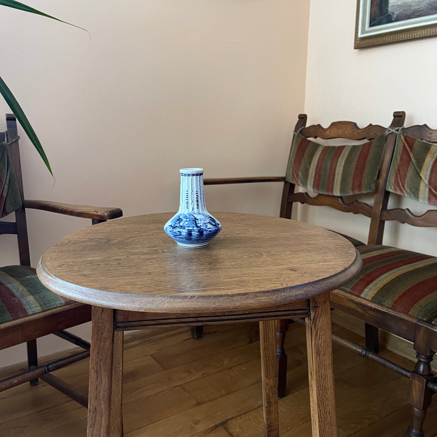 Round wooden table with a blue and white vase in a room with striped chairs.