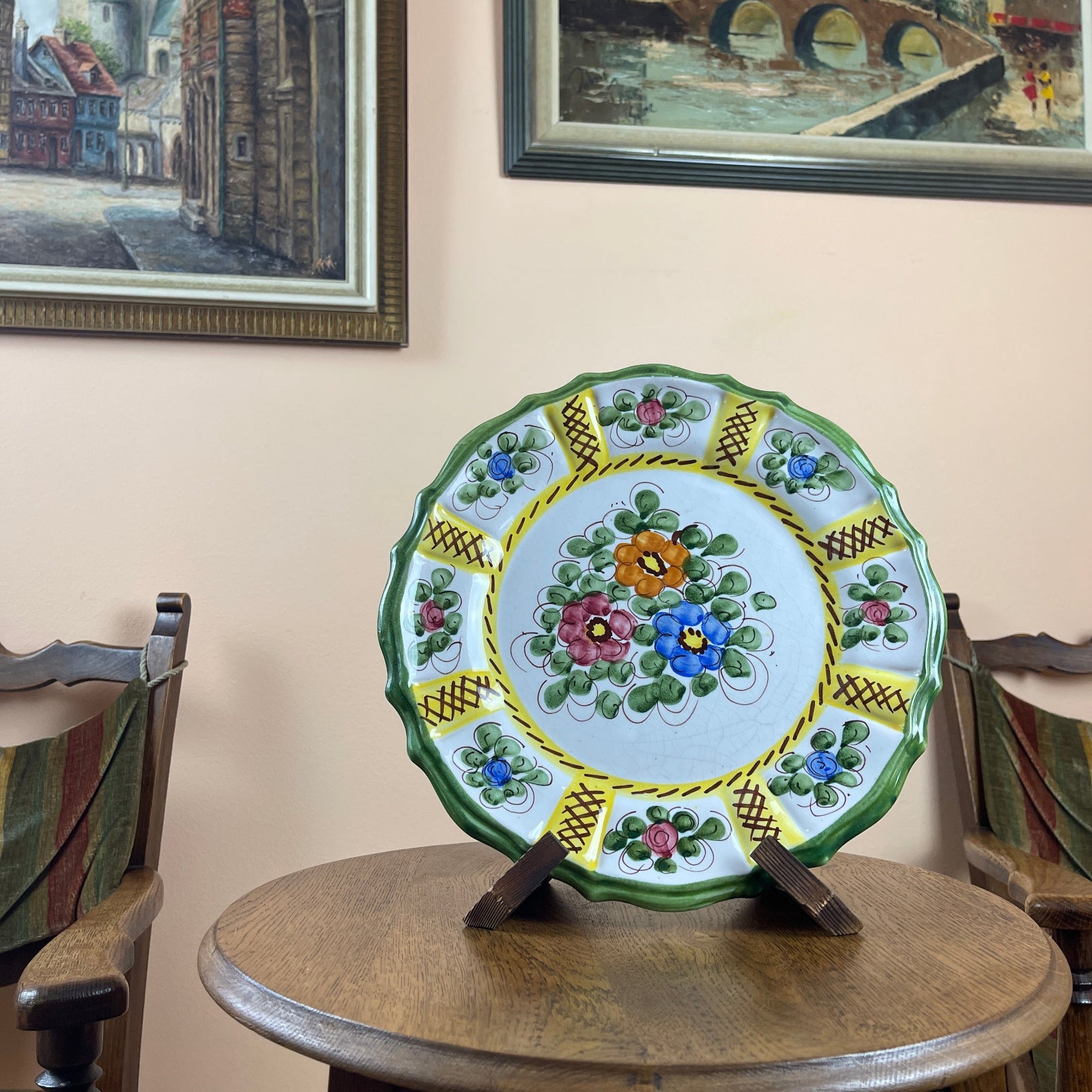 Decorative ceramic plate with floral patterns on a wooden table, framed pictures in the background