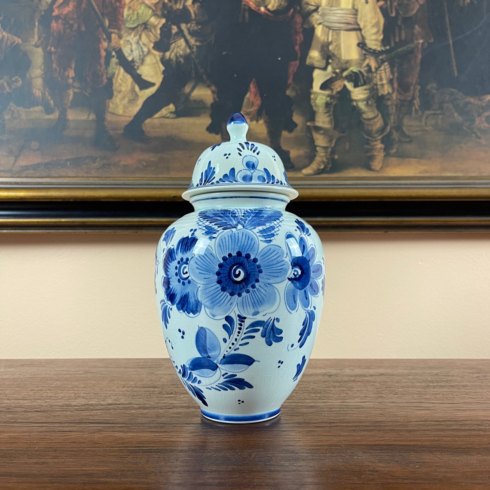 Blue and white floral ceramic jar on a wooden surface with a painting in the background