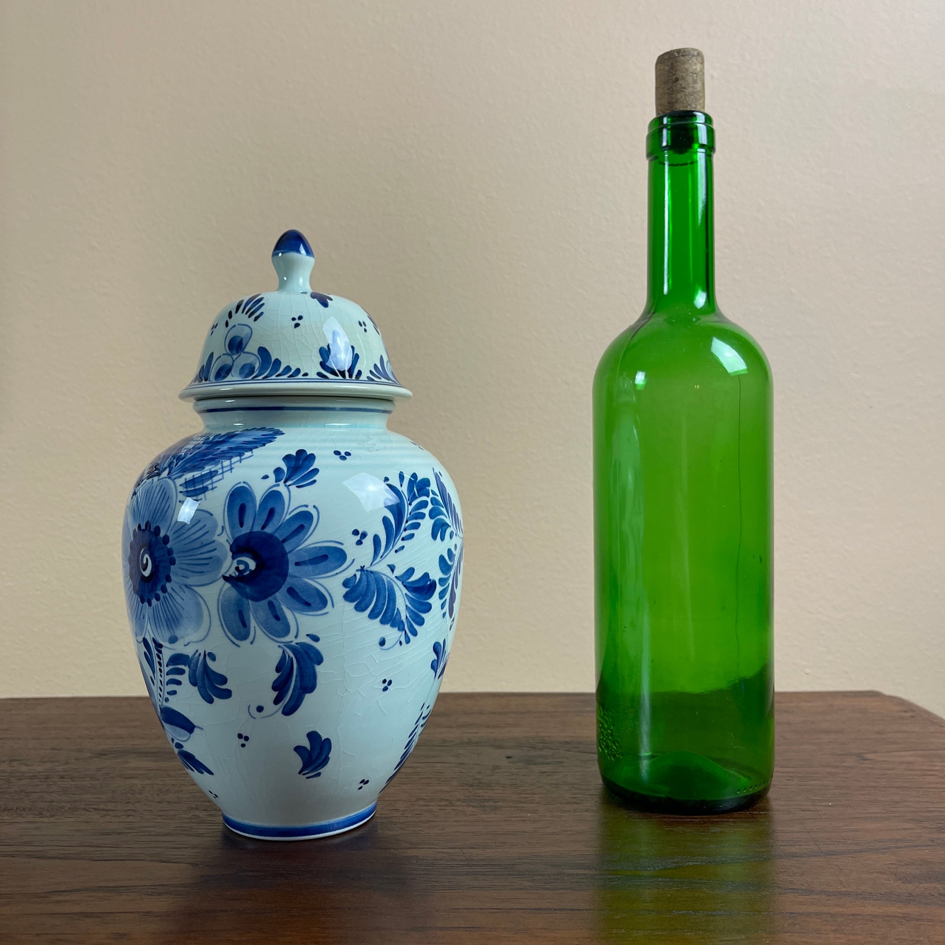 Blue and white floral-patterned jar next to a green bottle on a wooden surface with a beige background