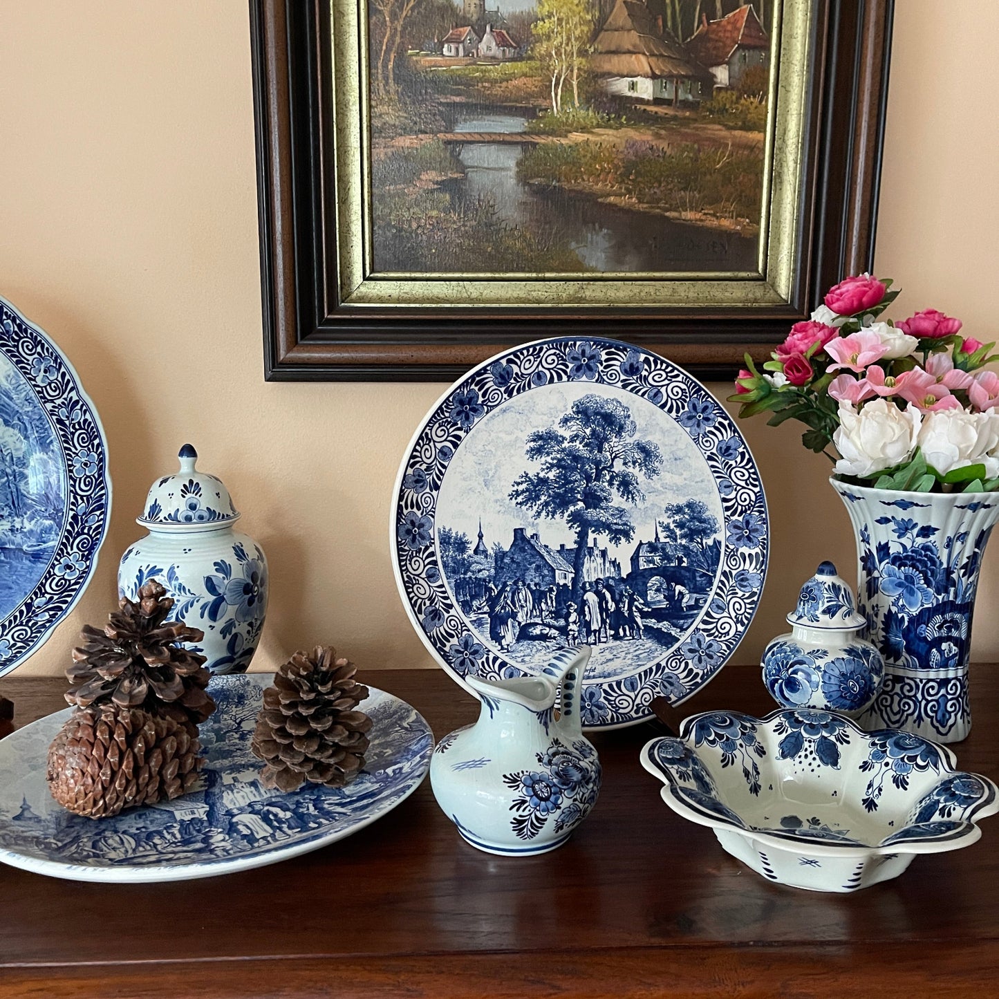 Collection of blue and white ceramic items on a wooden surface with a painting in the background.