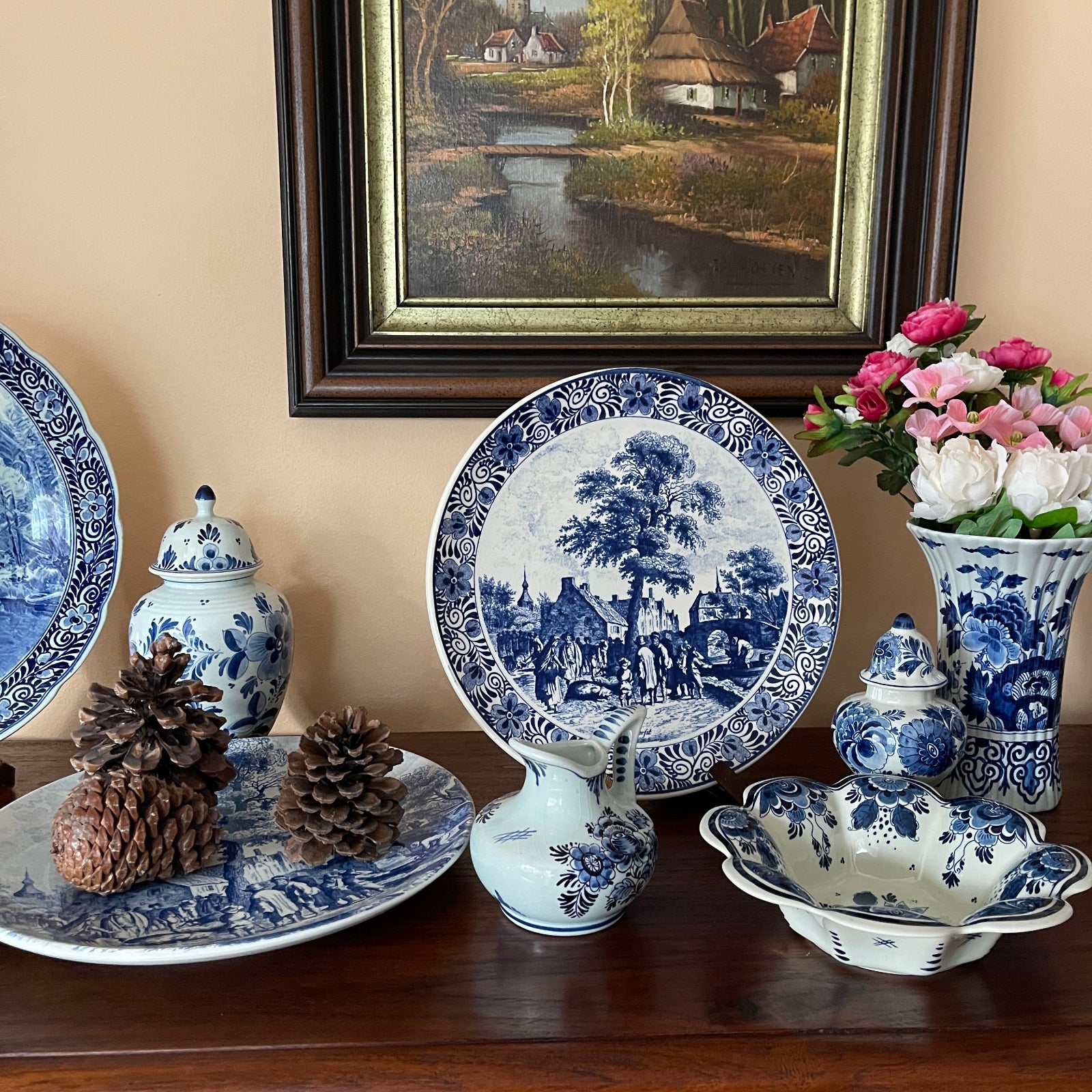 Collection of blue and white ceramic items on a wooden surface with a painting in the background.
