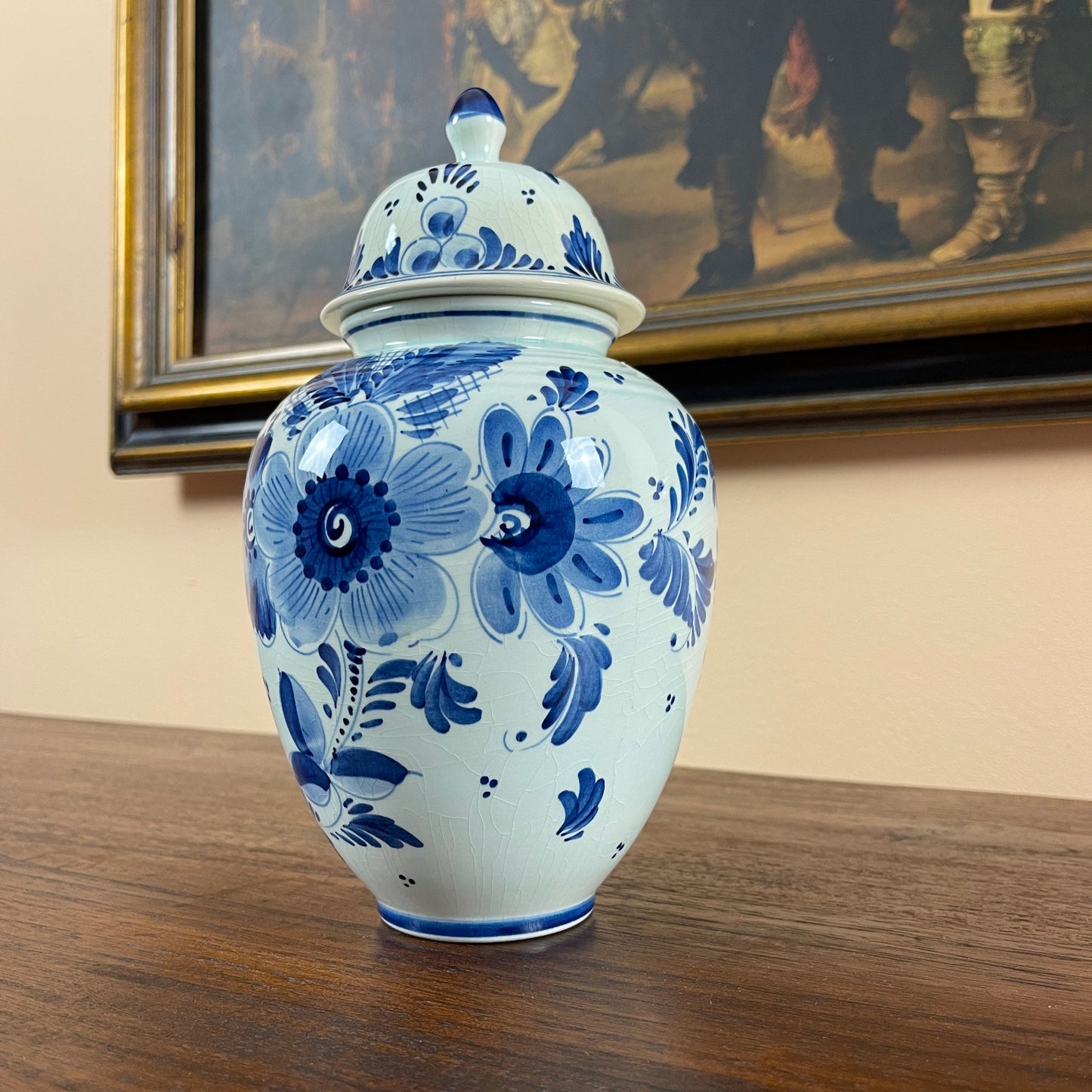 Blue and white floral ceramic jar on a wooden surface with a painting in the background