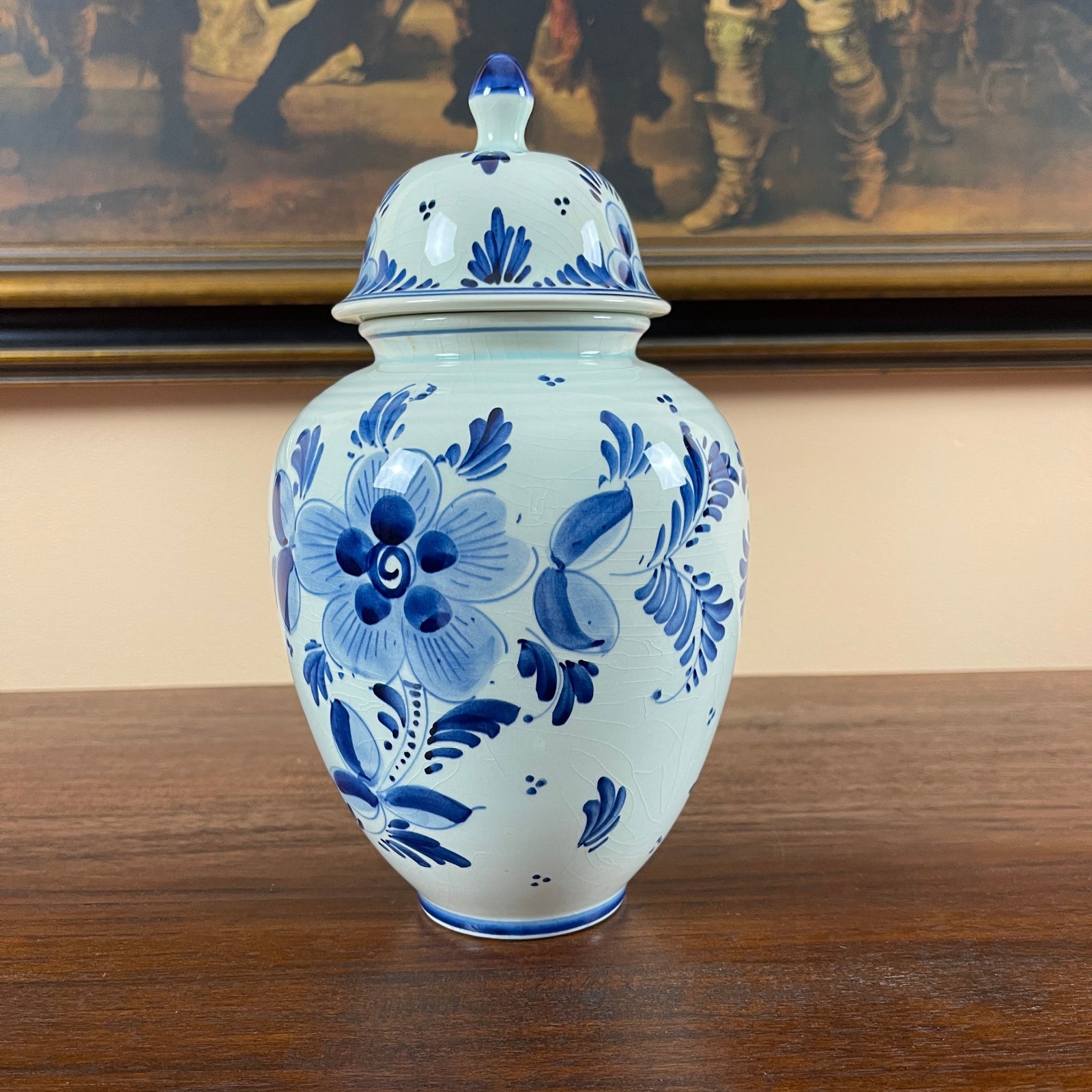 Blue and white floral ceramic jar on a wooden surface with a painting in the background