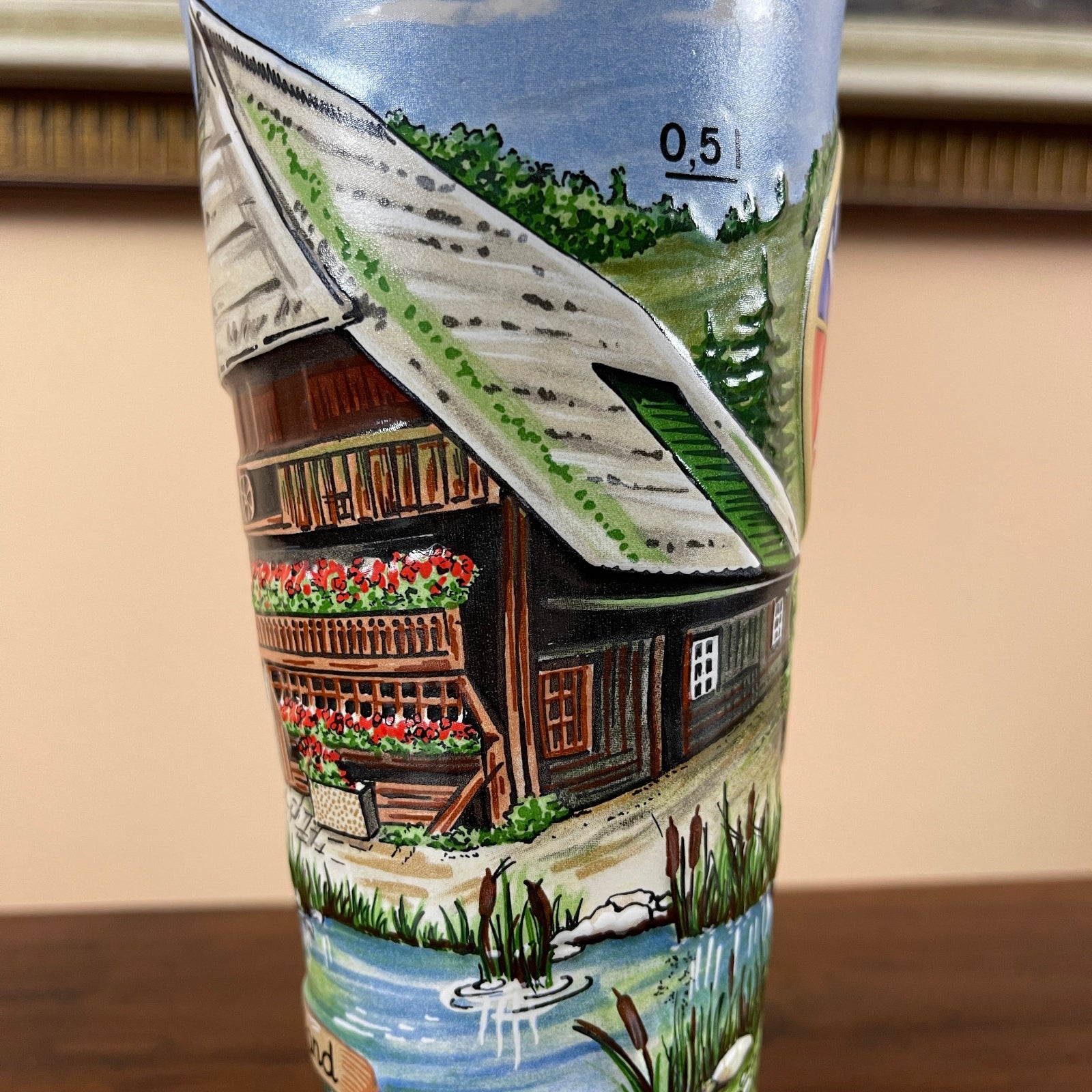 Decorative bottle with a painted scene of a cabin and garden on a neutral background