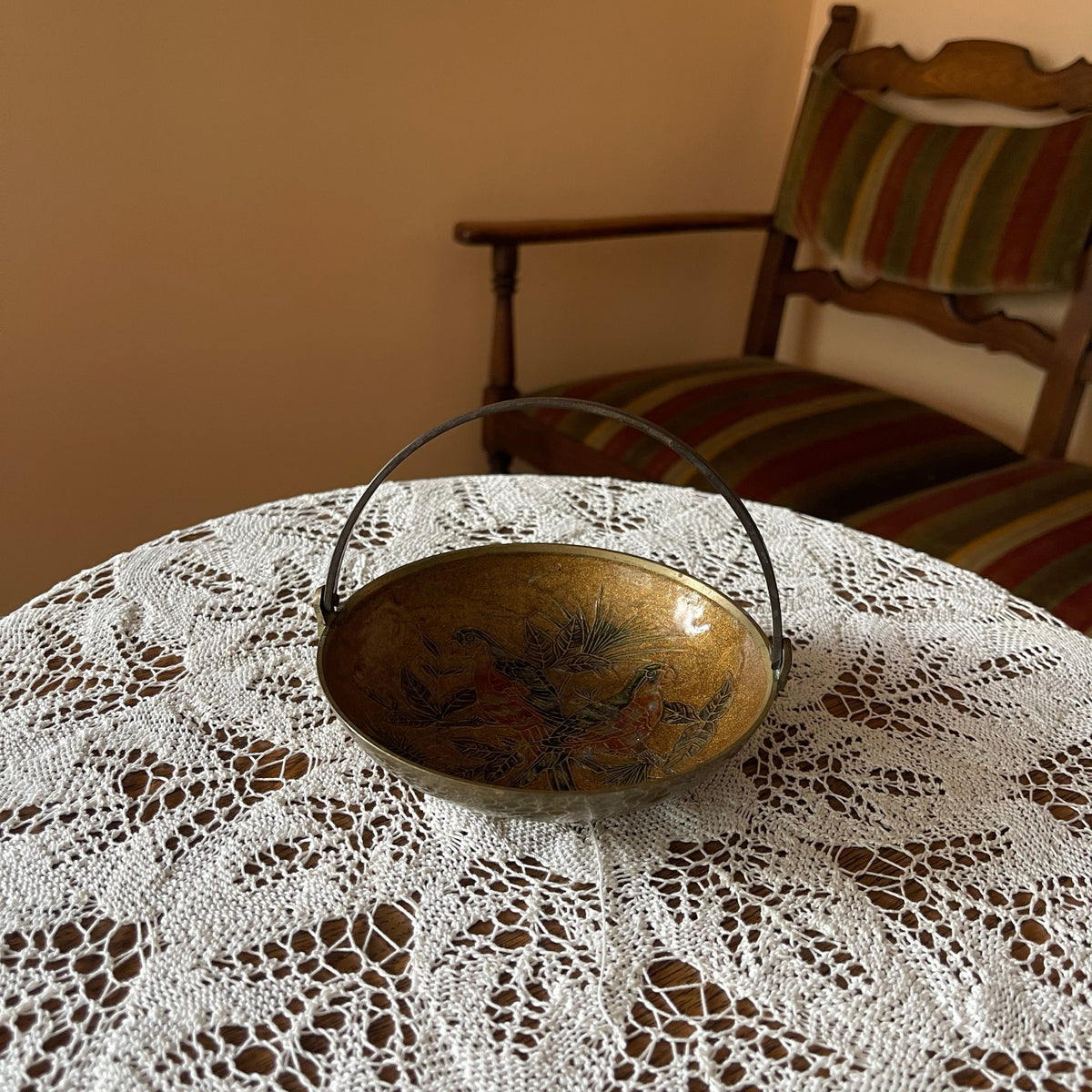 Decorative metal bowl on a lace tablecloth with a striped chair in the background