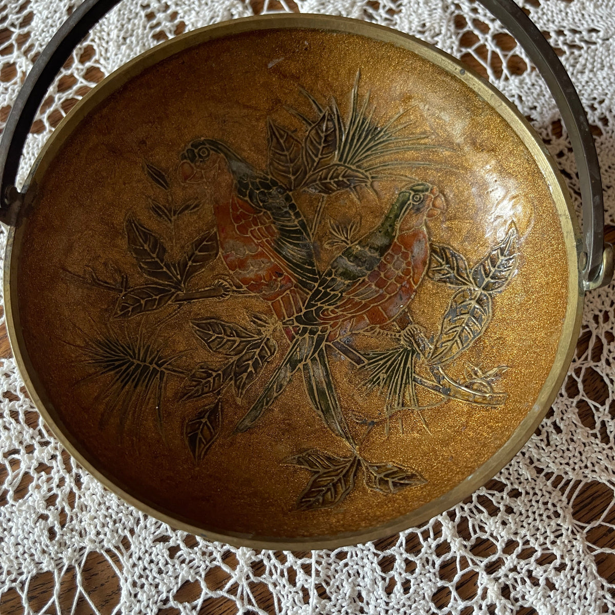 Decorative metal dish with bird and leaf design on a lace tablecloth
