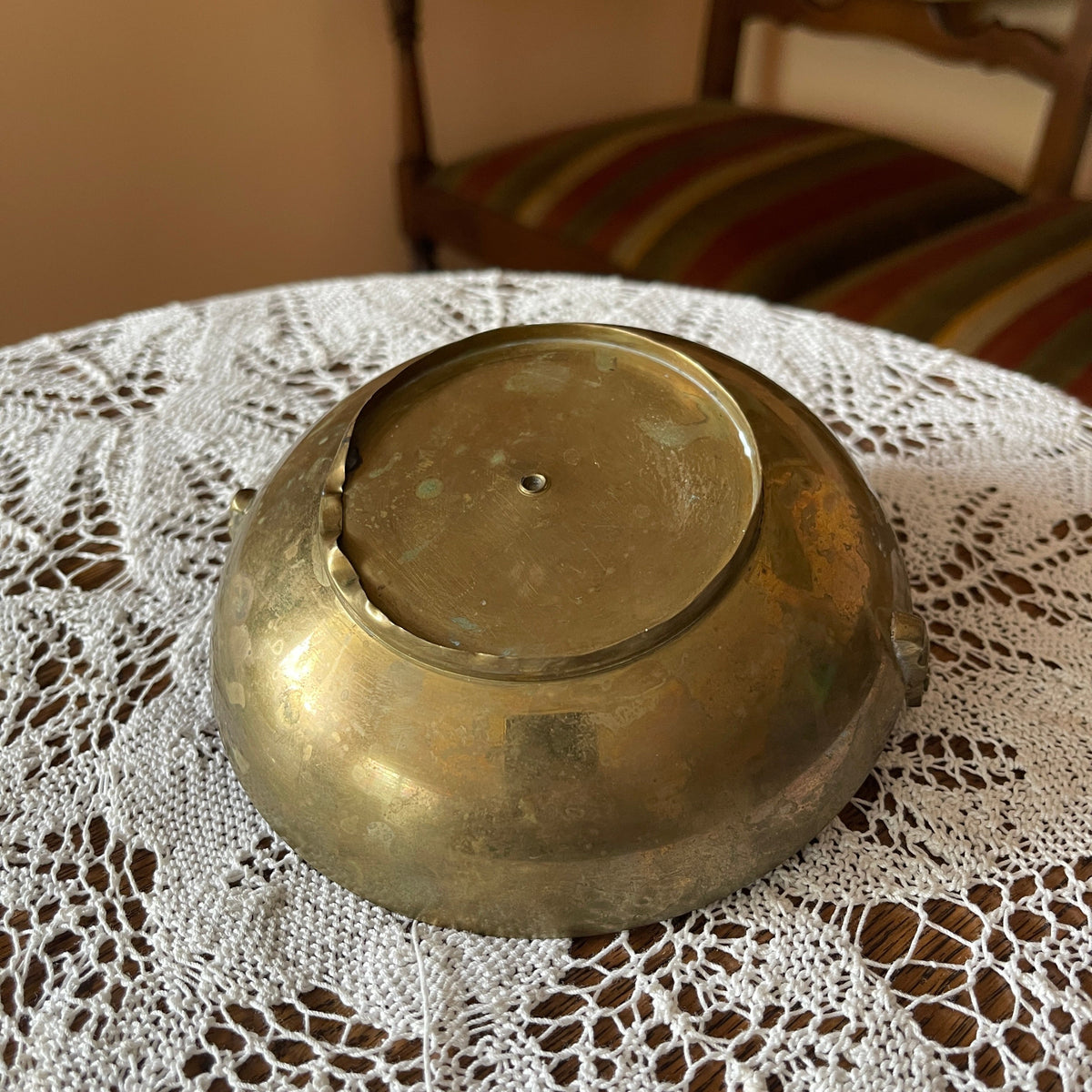 Brass bowl on a lace tablecloth with a striped cushion in the background