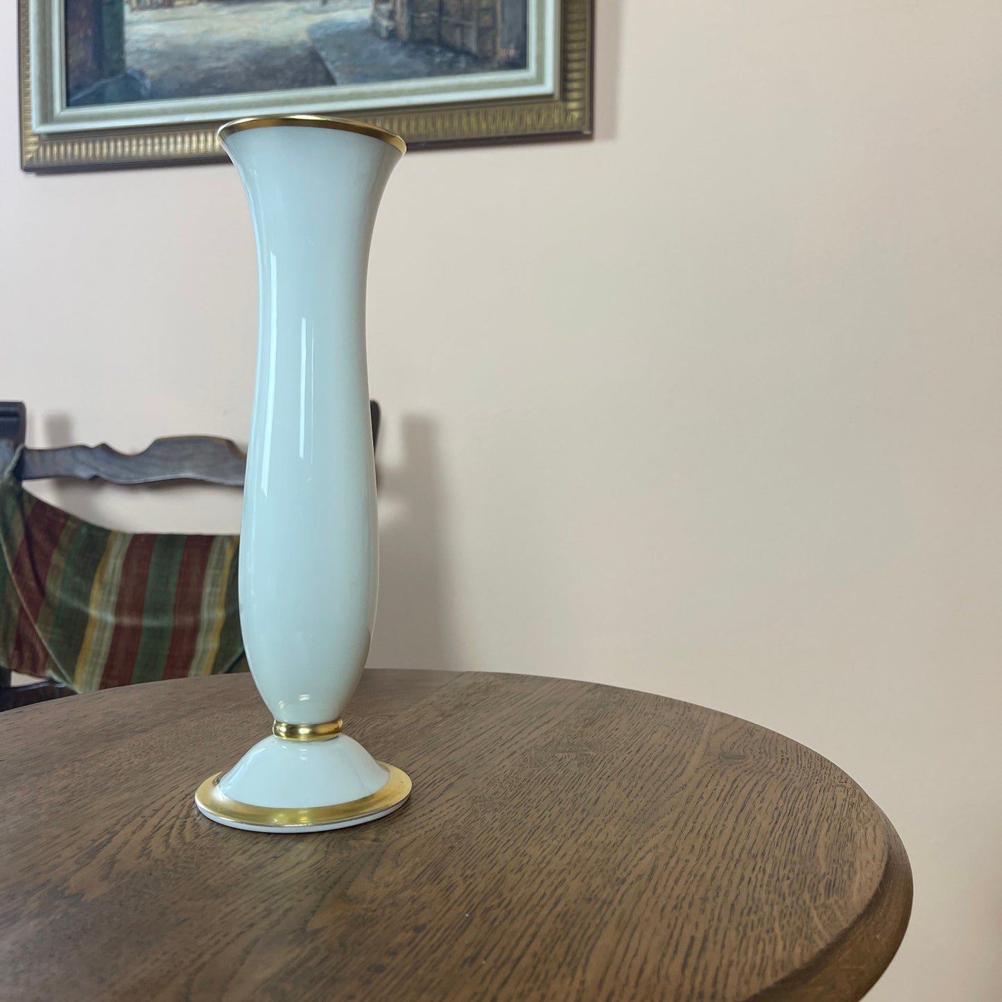 White vase with gold accents on a wooden table, framed picture in the background