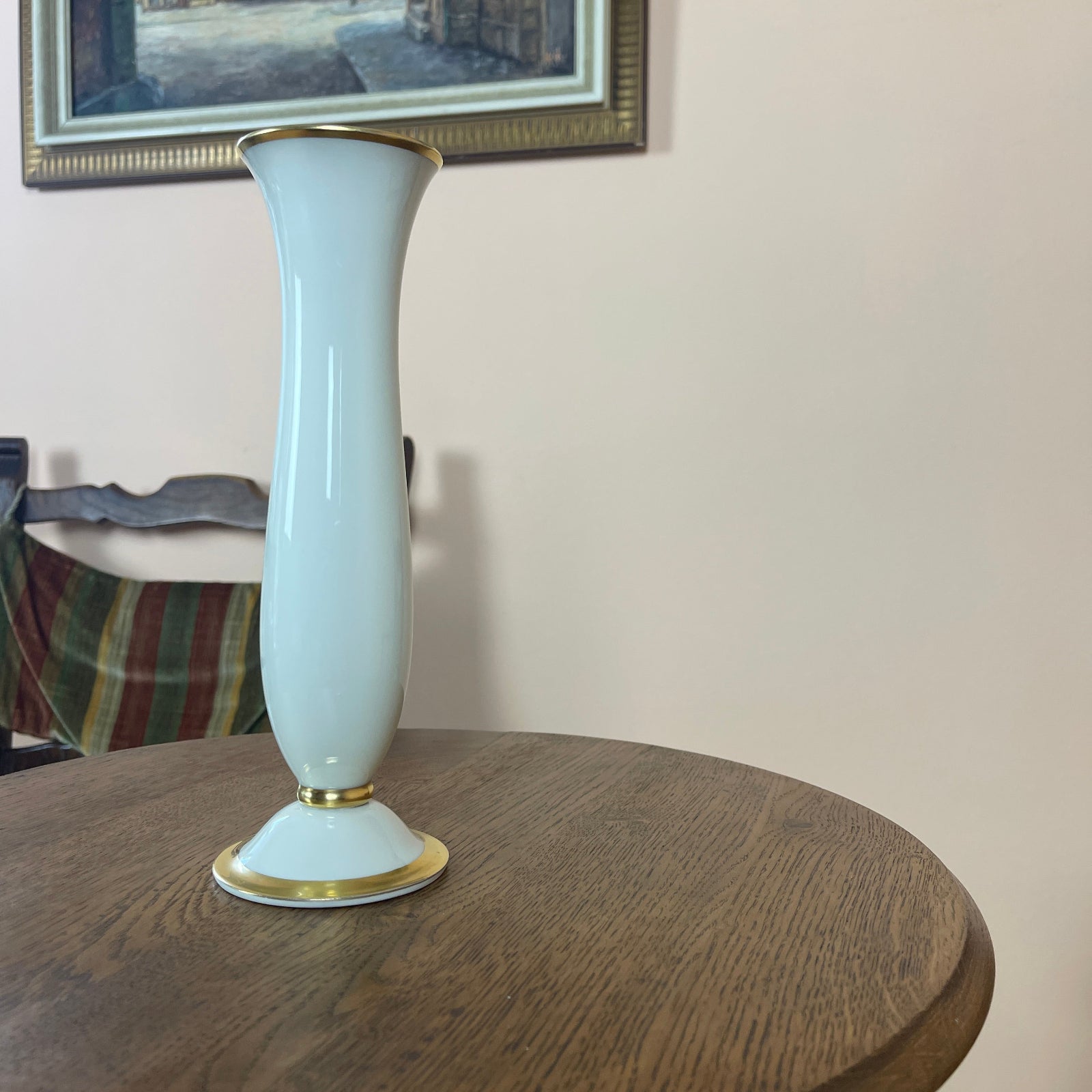 White vase with gold accents on a wooden table, framed picture in the background