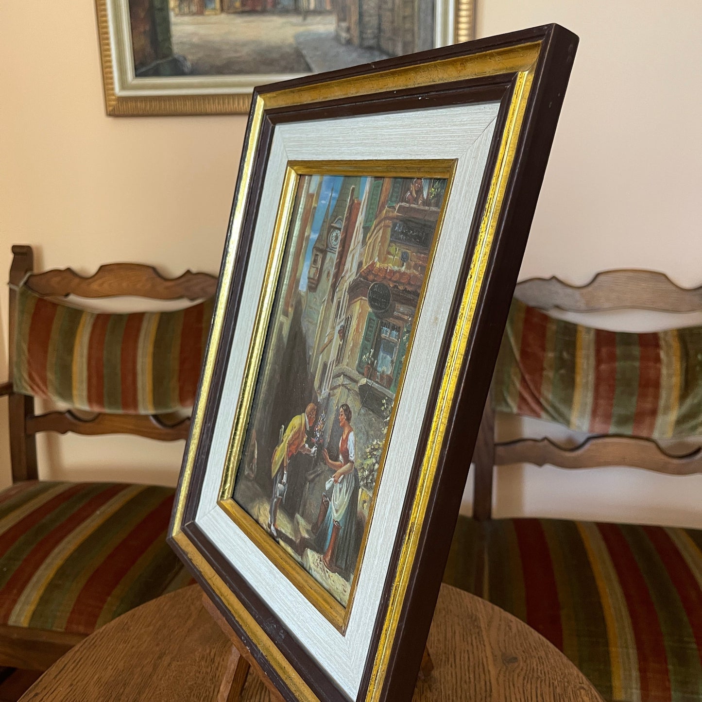 Framed painting on a table with striped chairs and a mirror in the background