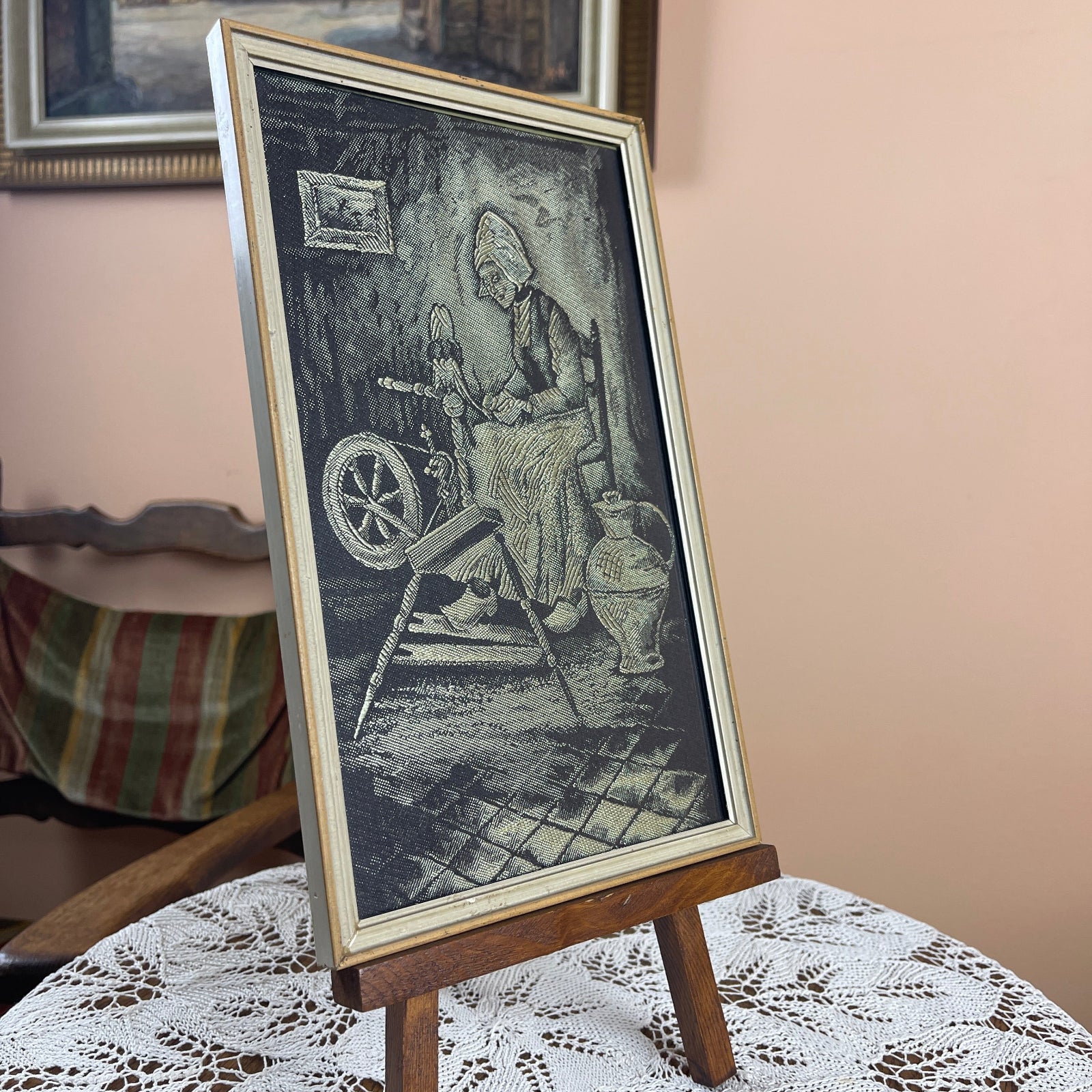 Vintage-style illustration of a woman at a spinning wheel on a stand with a lace tablecloth background.