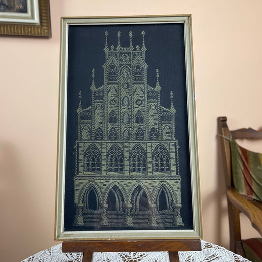 Framed artwork of a gothic cathedral on a table with a chair in the background.
