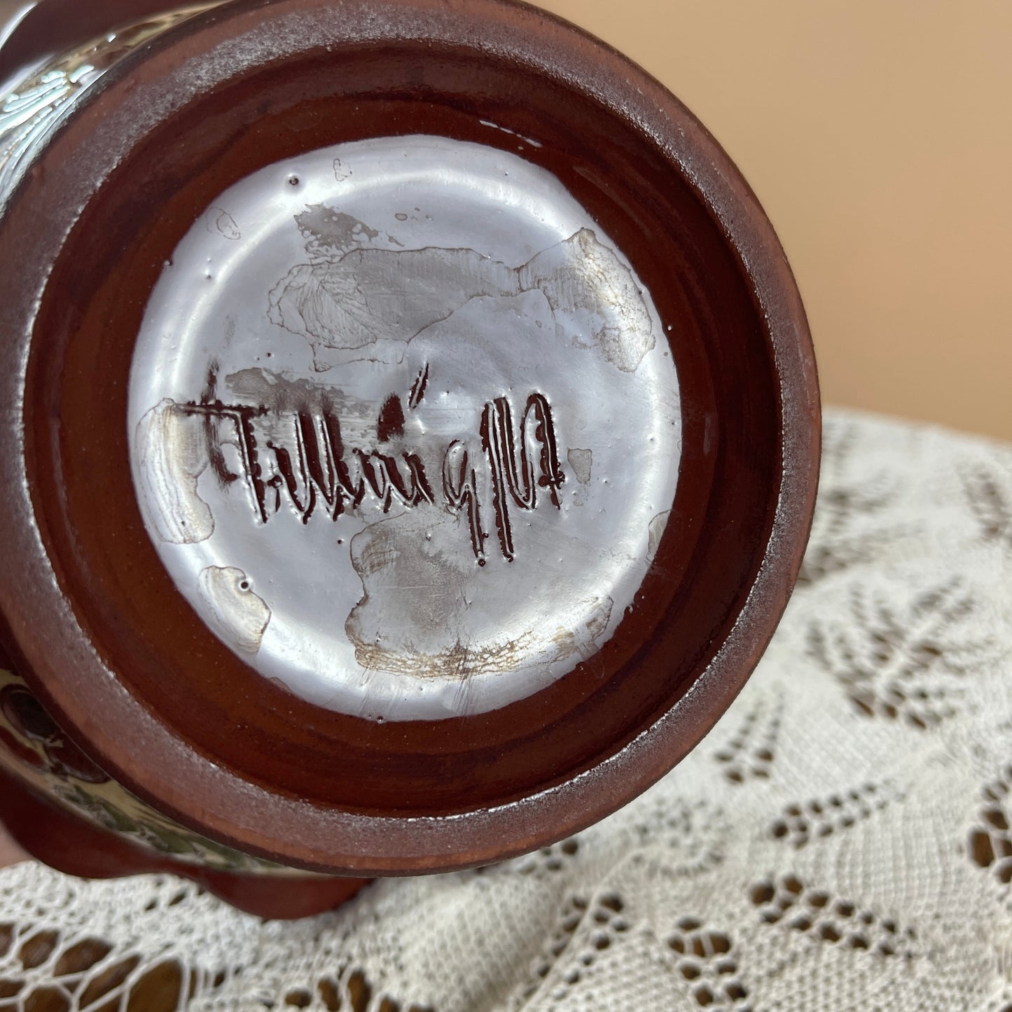 Close-up of a ceramic item with a signature on a lace tablecloth
