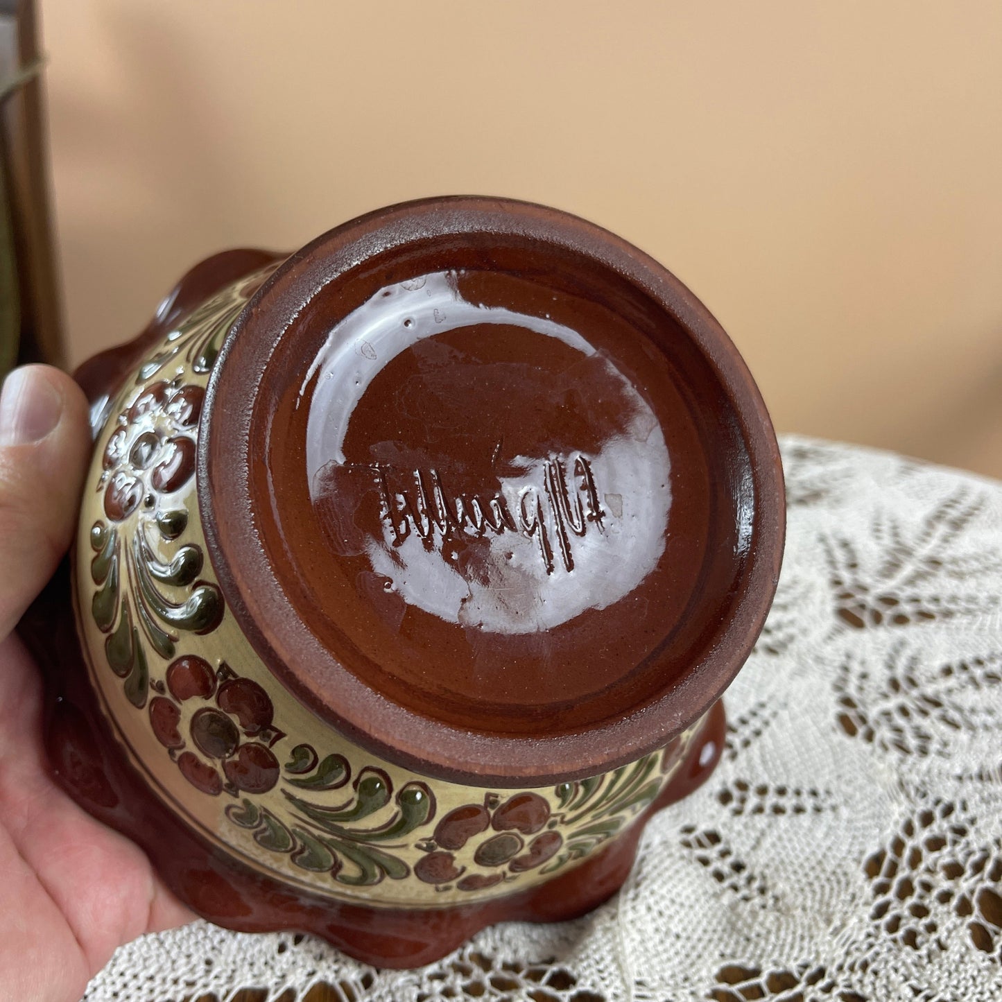 Decorative ceramic vase with floral patterns held by a hand on a lace tablecloth.