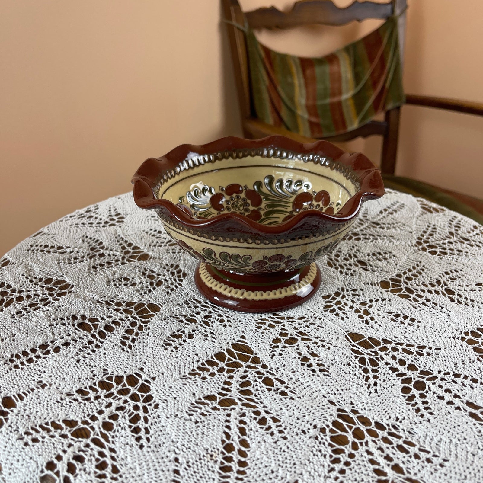 Decorative ceramic bowl on a lace tablecloth with a chair in the background