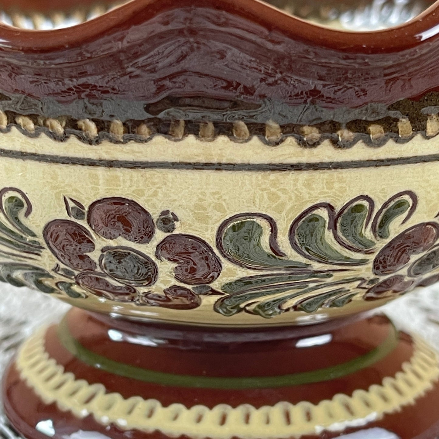 Close-up of a ceramic bowl with decorative brown and green patterns on a beige background.