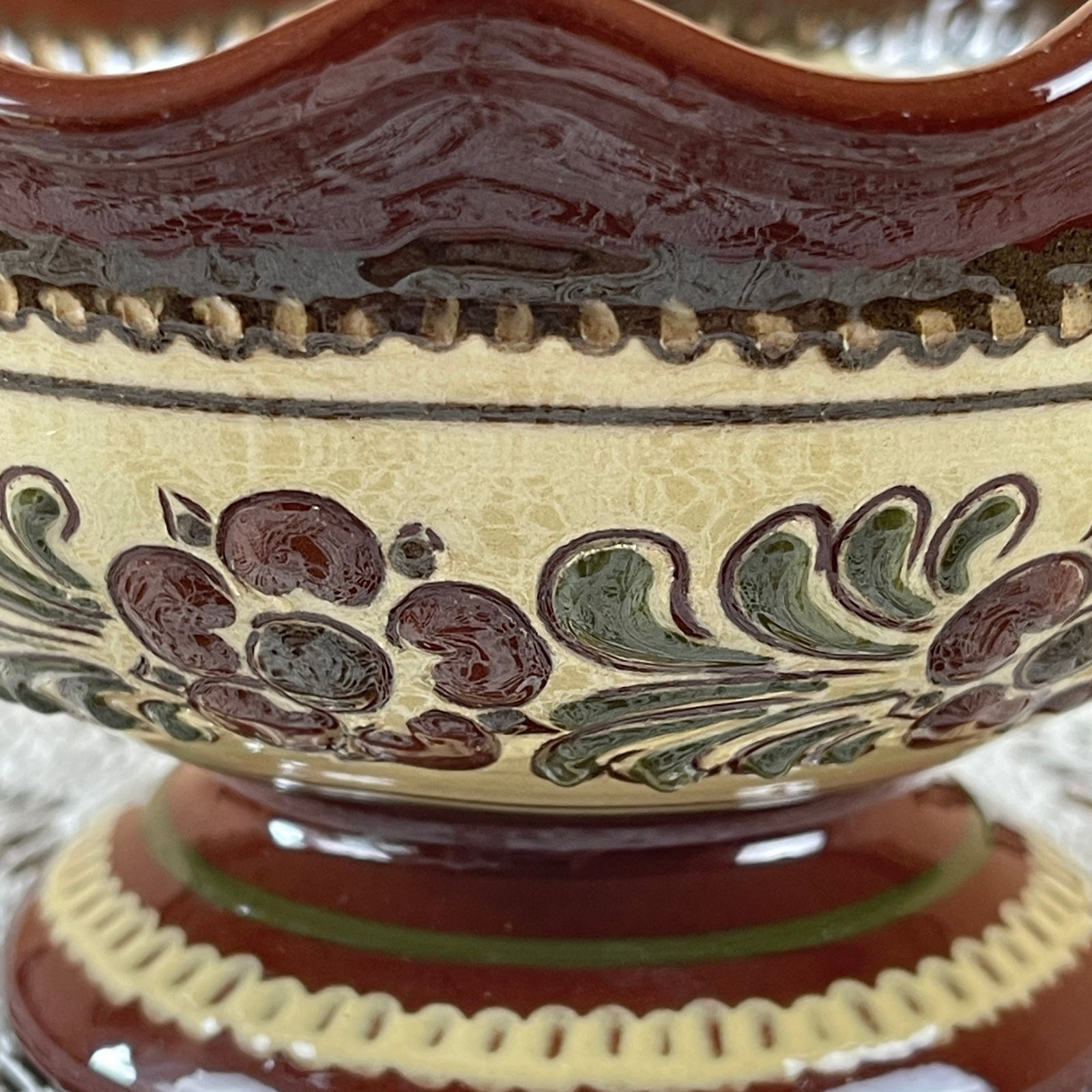Close-up of a ceramic bowl with decorative brown and green patterns on a beige background.
