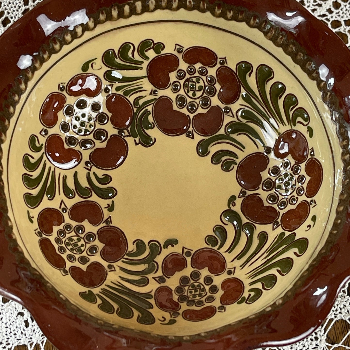 Ceramic plate with decorative brown and green pattern on a beige background