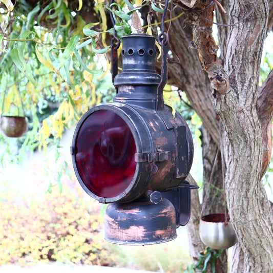 Vintage oil signal lantern with a milky white glass cover and red and orange acrylic glass panels, hanging from a tree.