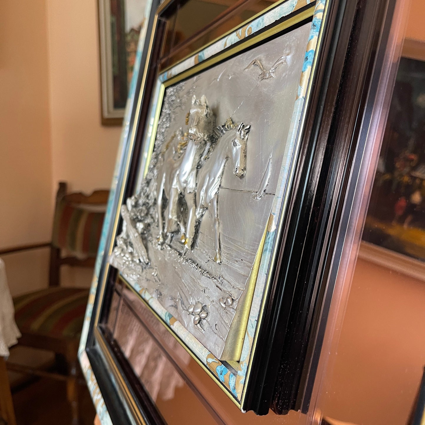 Decorative plaque with horse and rider design in a gold frame, placed on a surface.