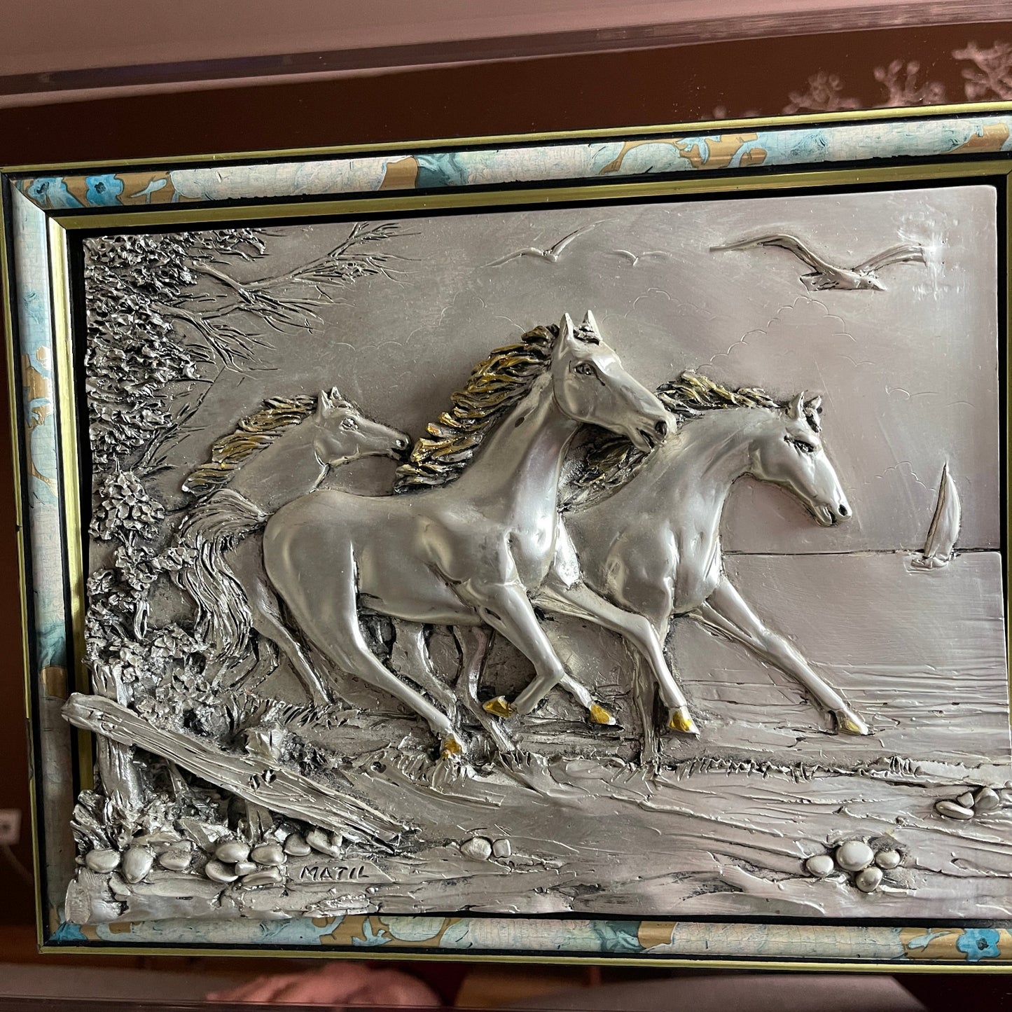 Decorative wall art with three horses running, framed in gold.