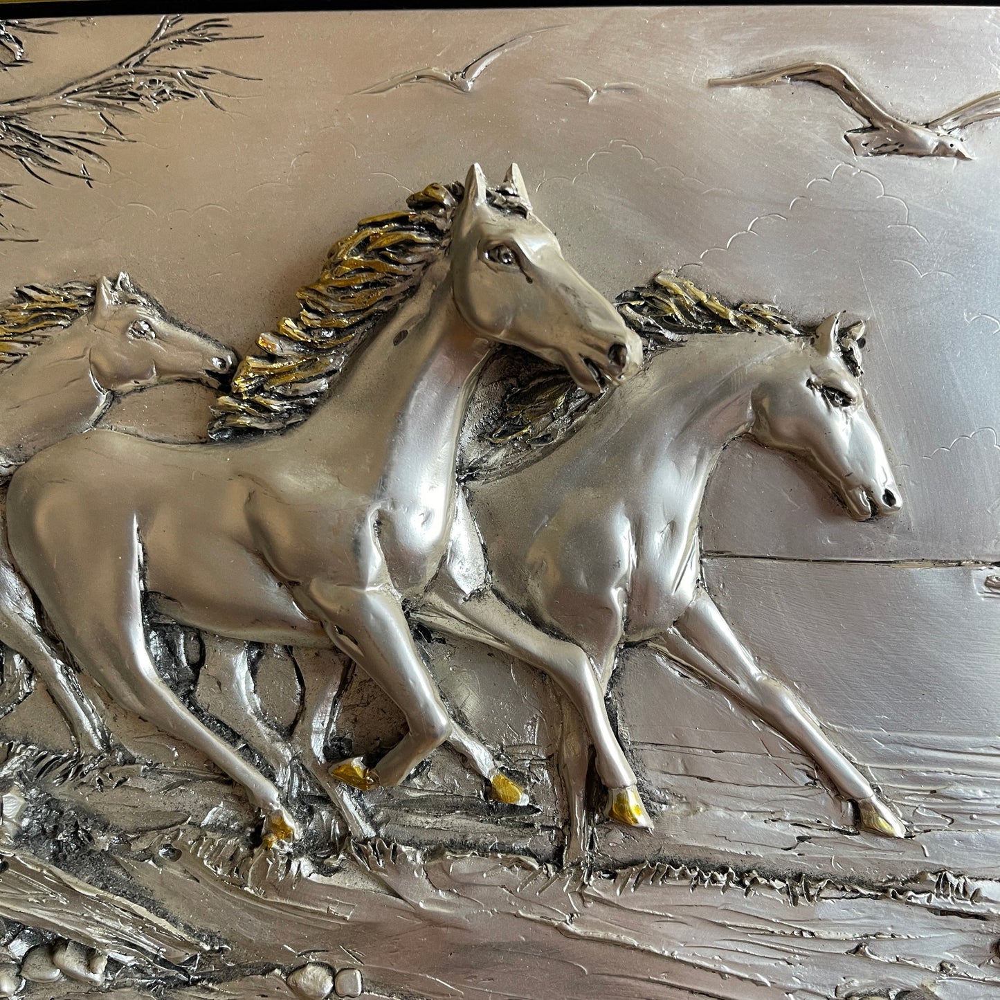 Metallic sculpture of three horses running on a textured surface