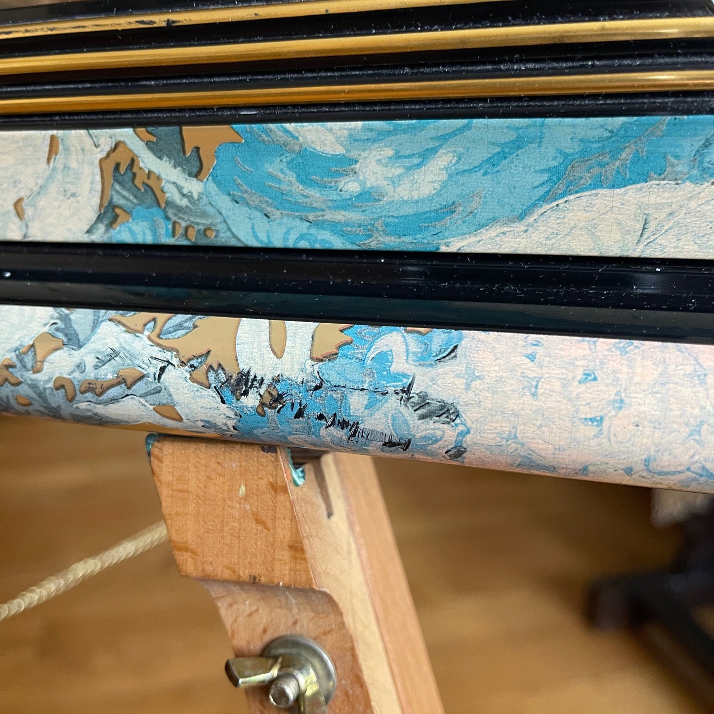 Close-up of a wooden frame with decorative paper and a black strip.
