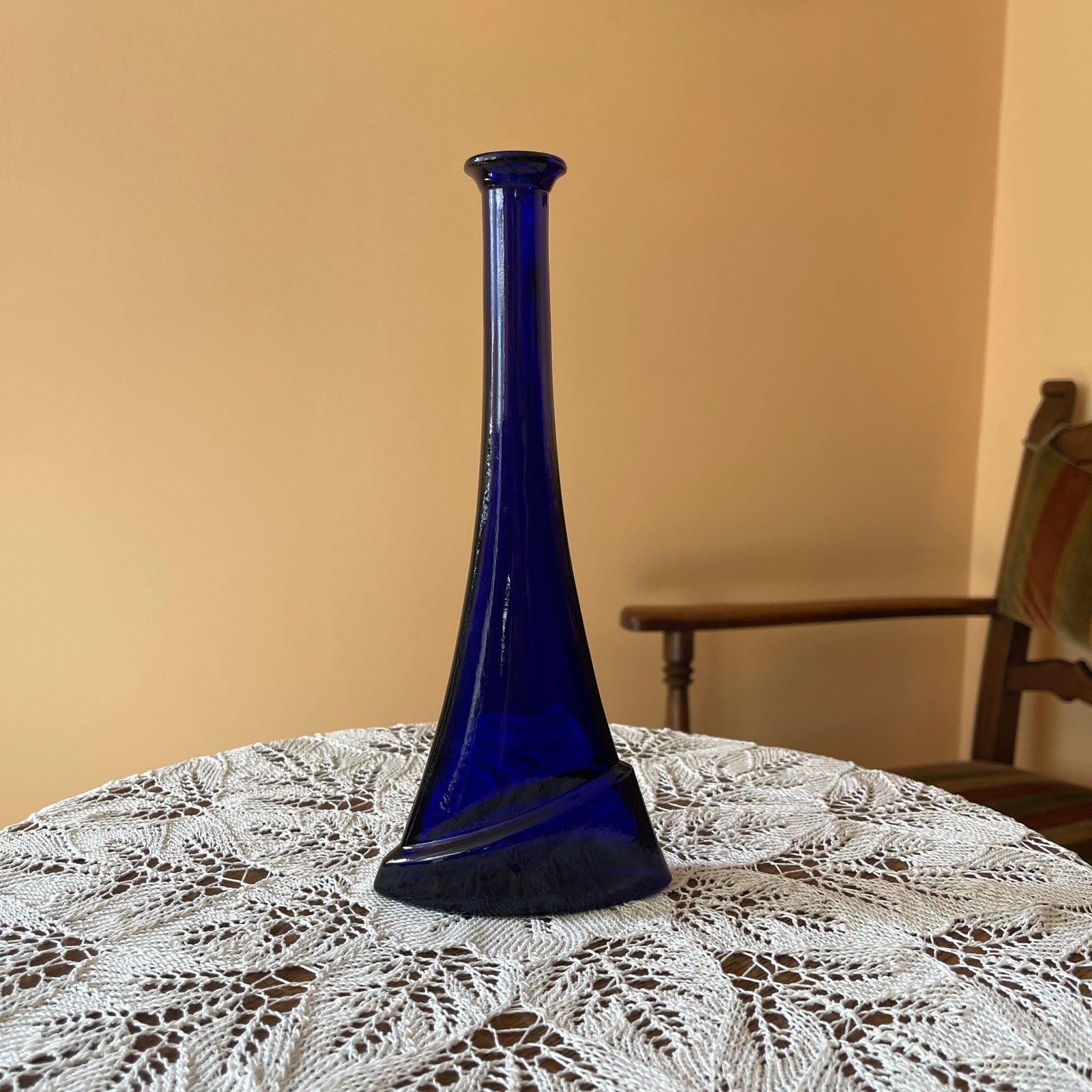 Blue vase on a lace tablecloth with a wooden chair in the background