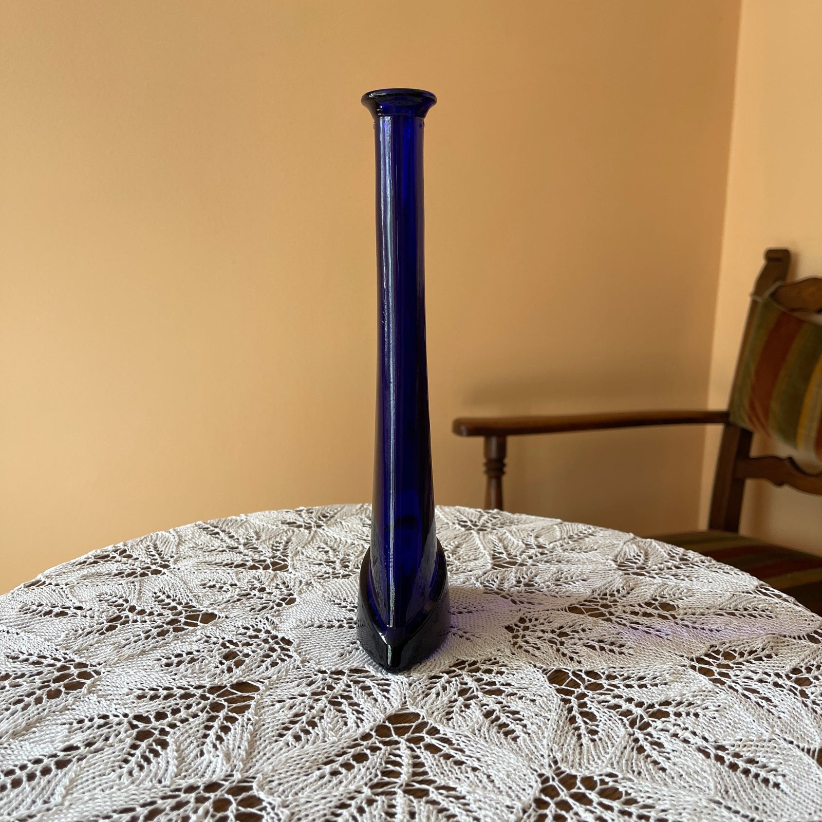 Blue vase on a lace tablecloth with a wooden chair in the background