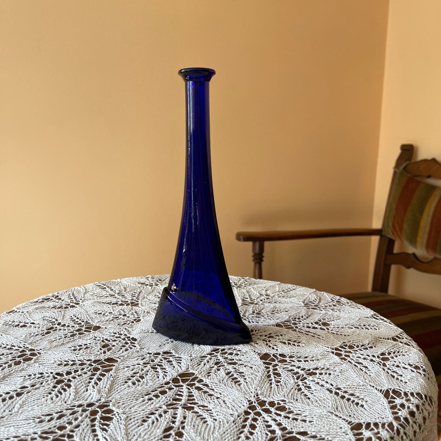 Blue vase on a lace tablecloth with a wooden chair in the background
