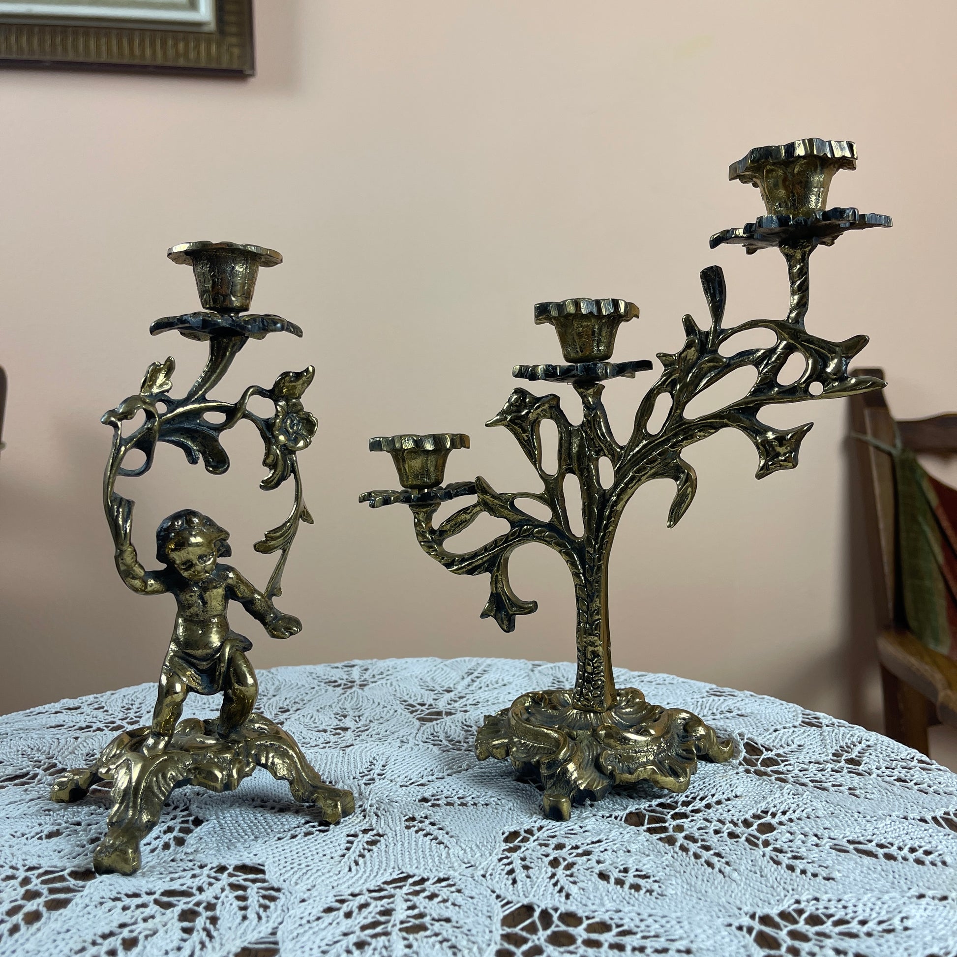 Two ornate brass candle holders on a lace tablecloth with a neutral background
