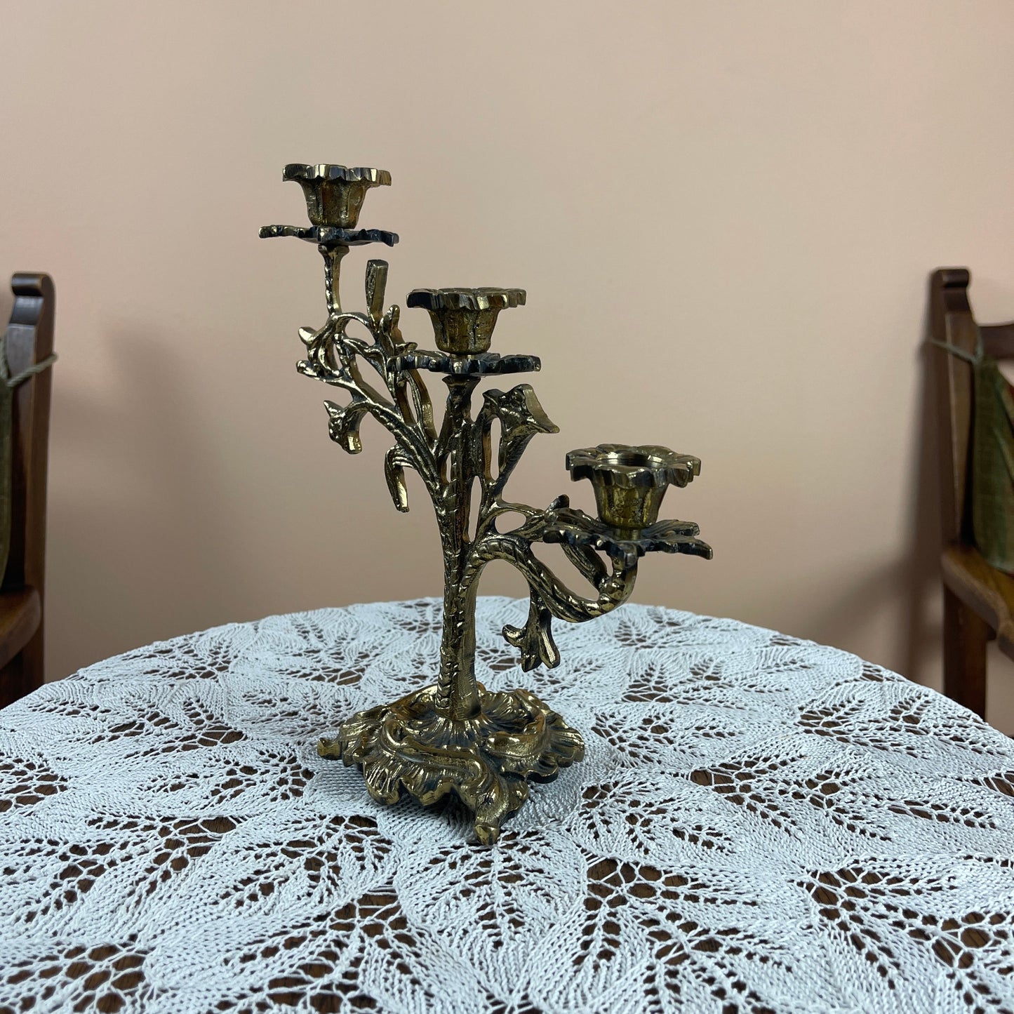 Decorative metal candelabra on a table with a lace tablecloth and chairs in the background.