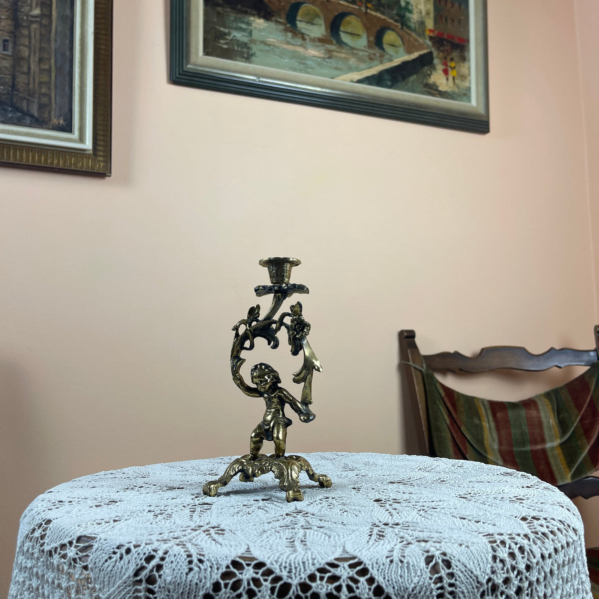 Decorative candle holder on a table with lace tablecloth, framed artwork in the background
