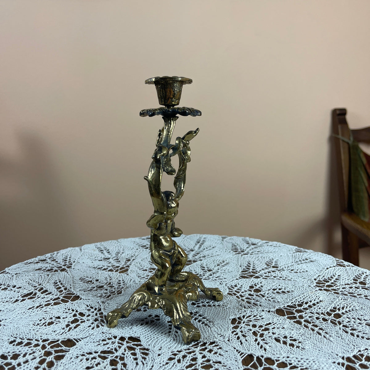 Decorative candle holder on a table with a lace tablecloth and wooden chair in the background.