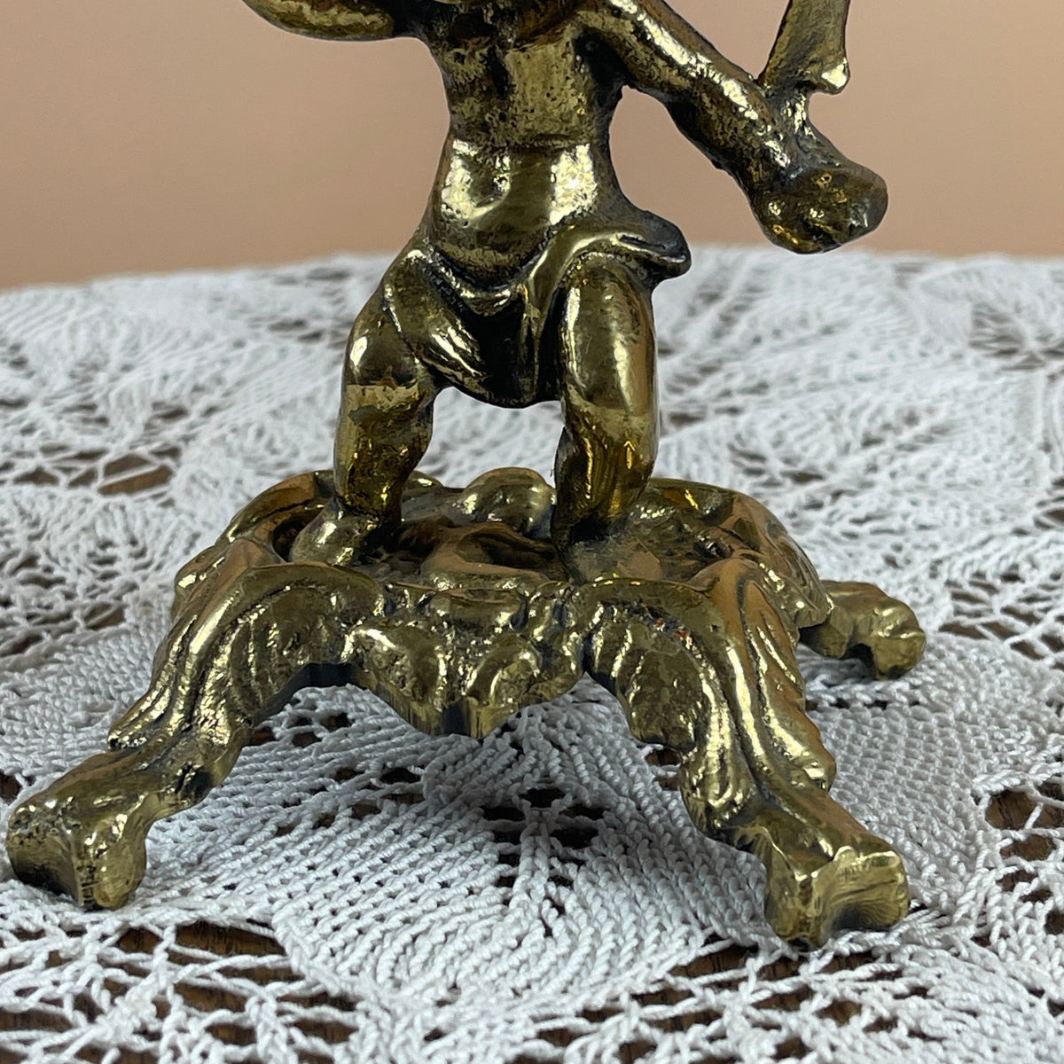 Bronze figurine of a standing figure on a lion's head on a lace tablecloth.