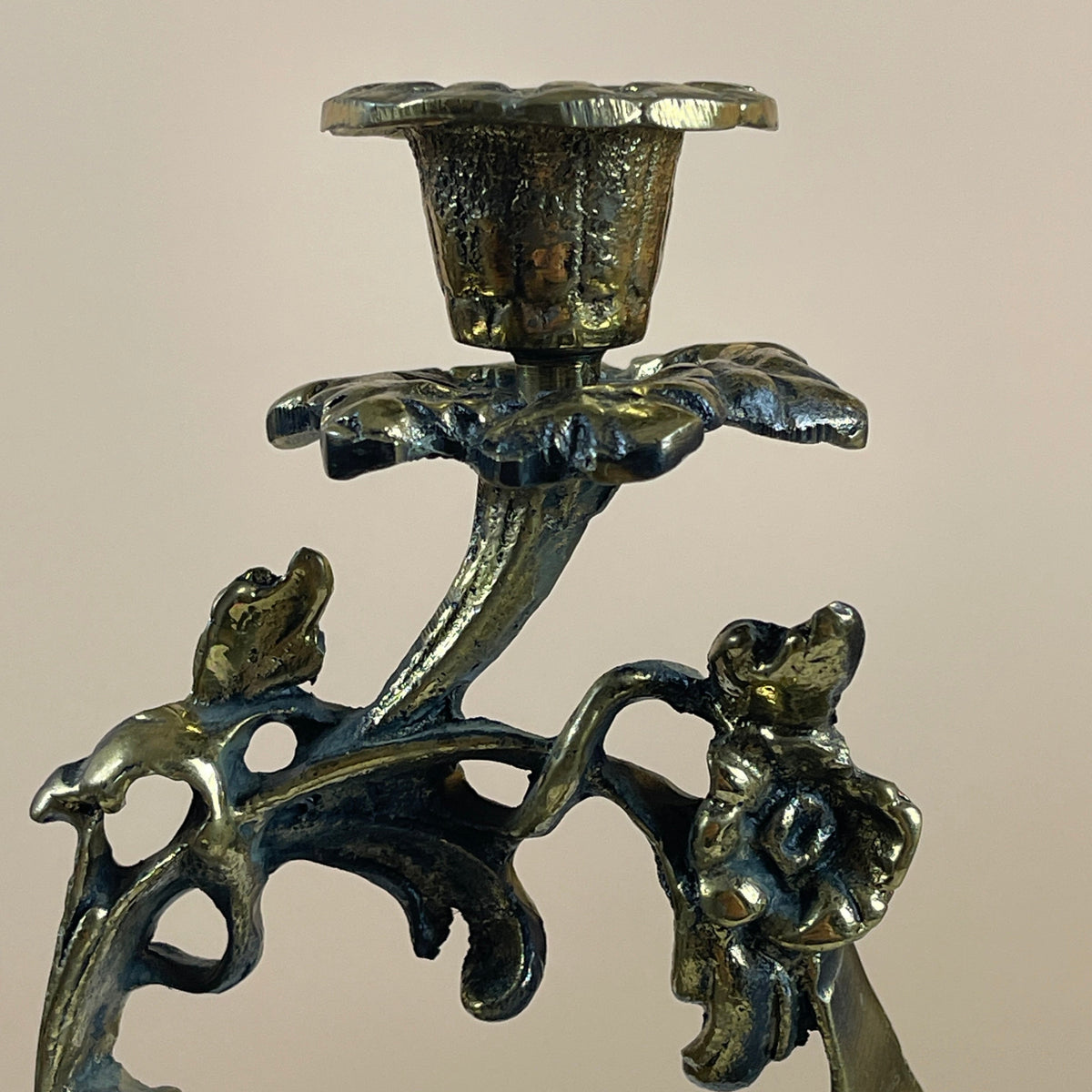 Bronze candle holder with floral design and two small figures on a beige background