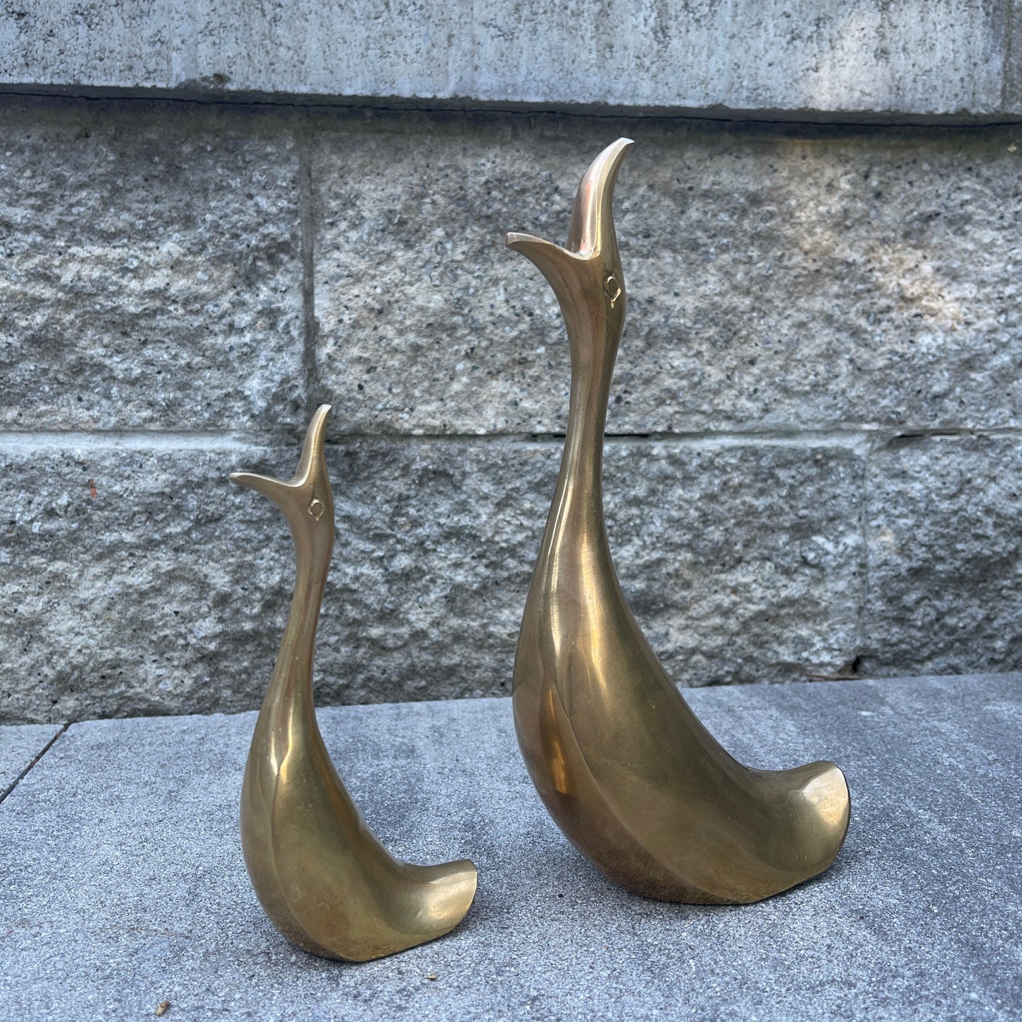 Two brass bird sculptures on a stone surface with a stone wall background