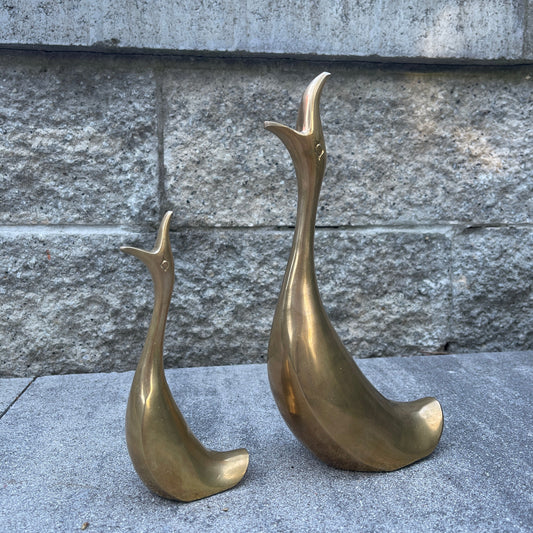 Two brass bird sculptures on a stone surface with a stone wall background