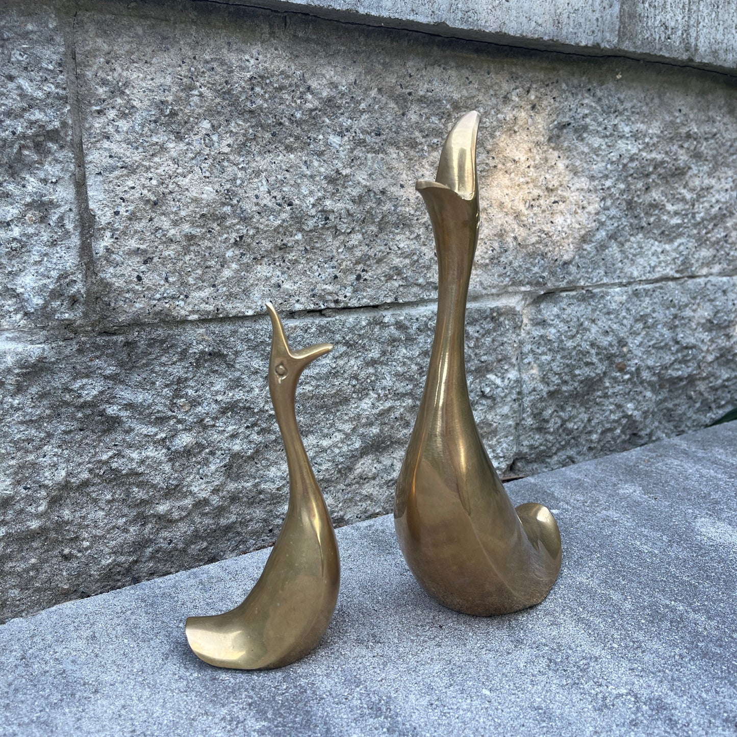Two brass duck sculptures on a stone surface with a stone wall background