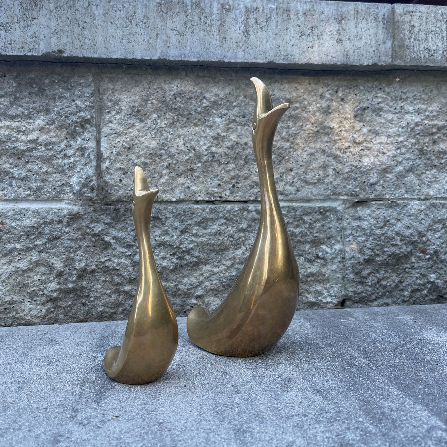 Two brass duck sculptures on a stone surface with a stone wall background