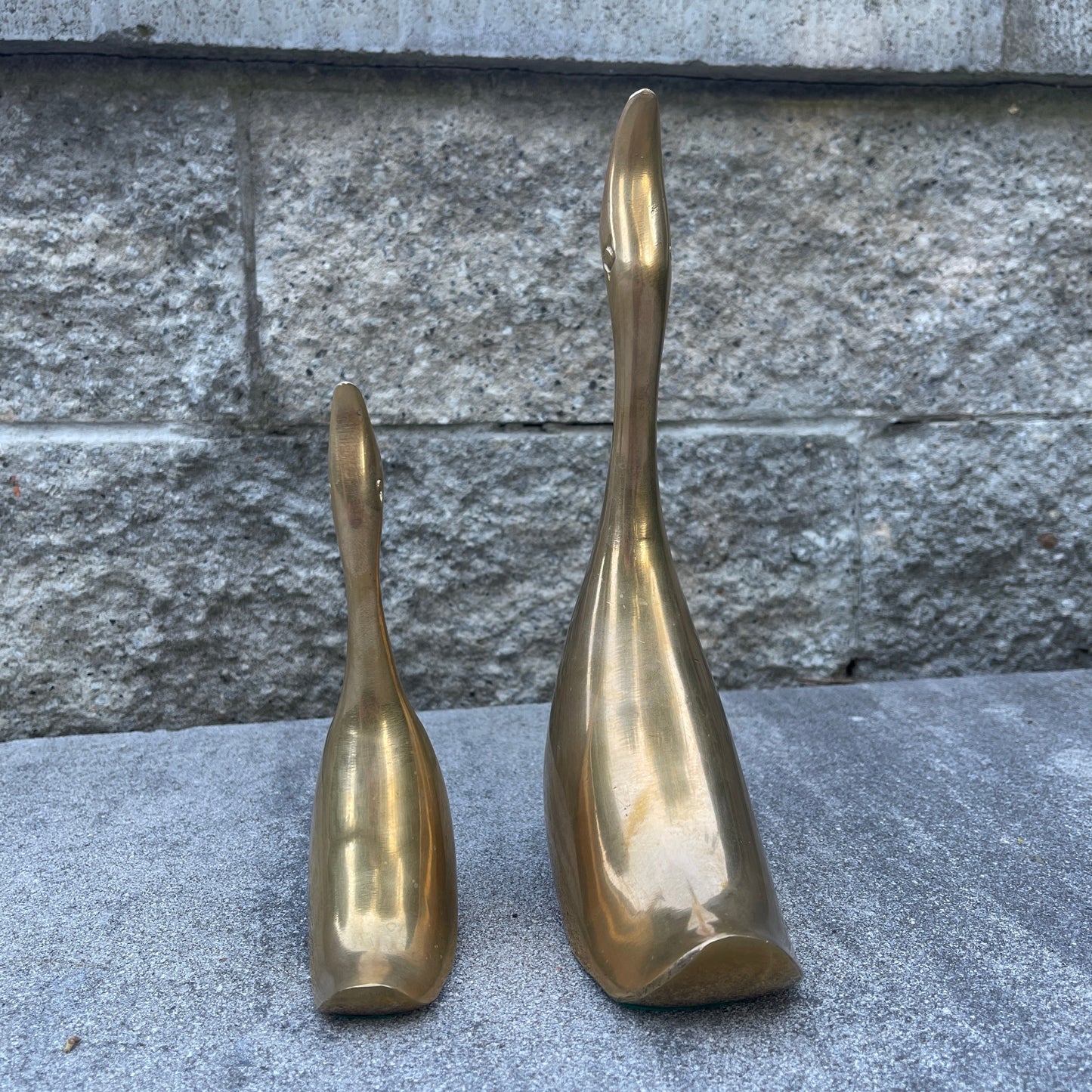 Two brass sculptures on a stone surface with a stone wall background