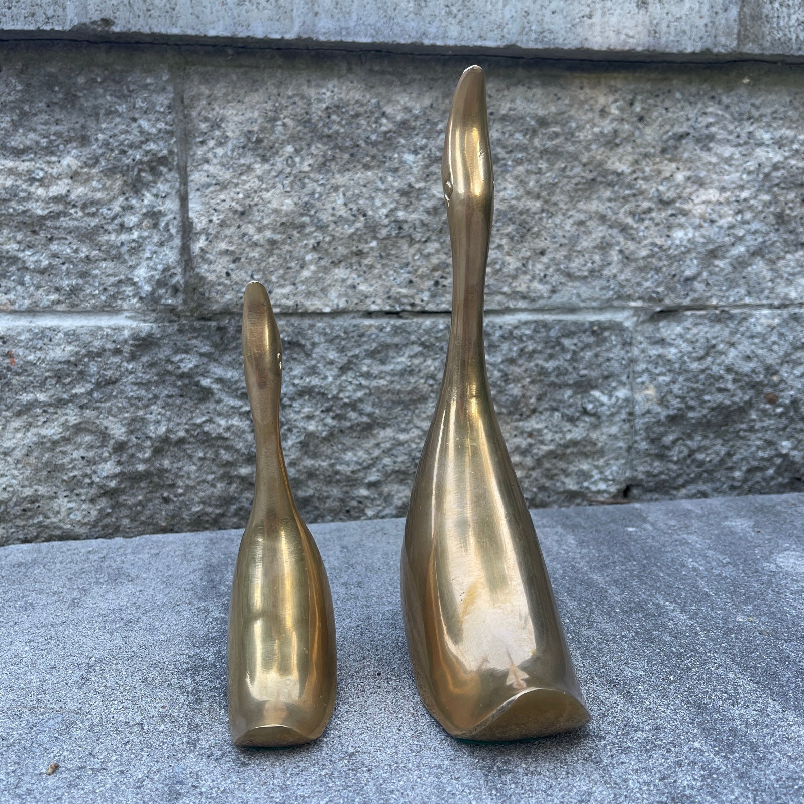 Two brass sculptures on a stone surface with a stone wall background